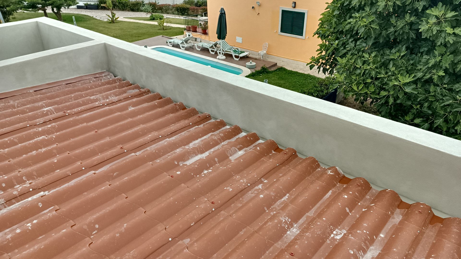Telhado de zinco vermelho com uma borda de concreto branco com vista para uma piscina e um prédio.