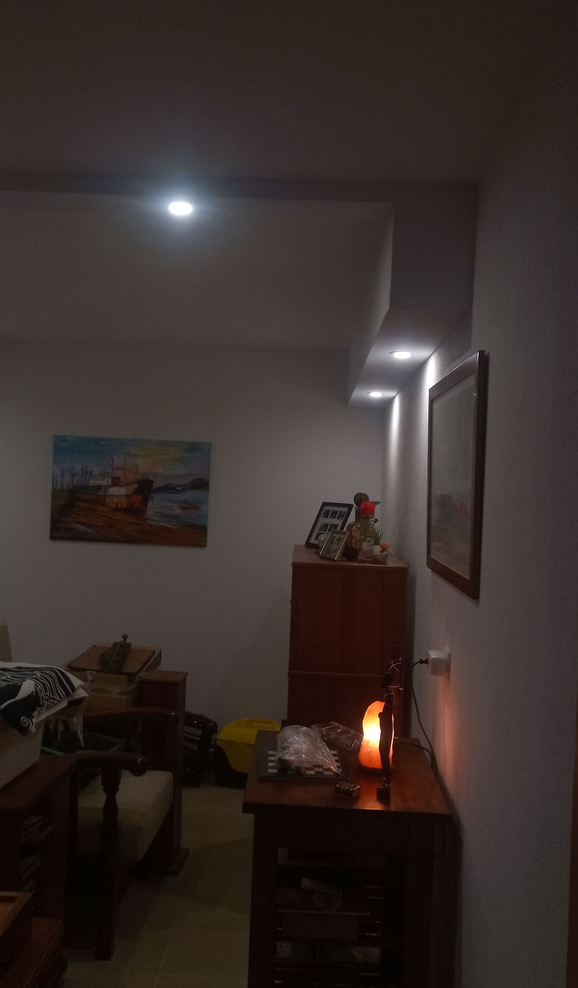 Interior de um quarto com pouca luz, contendo um quadro, armários, uma vela e luzes embutidas no teto.