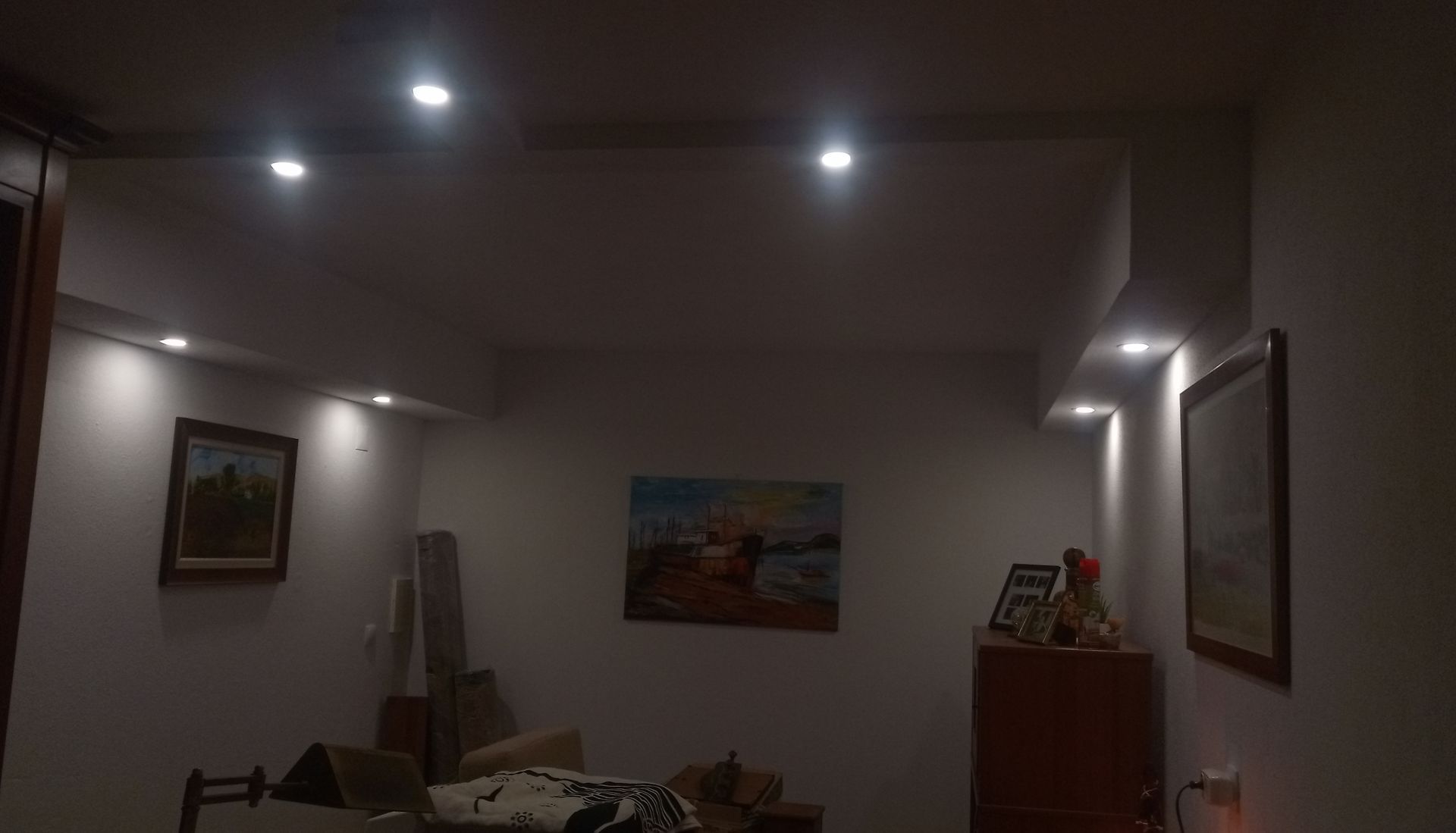 Um quarto com pouca luz, decorado com obras de arte, móveis e iluminação embutida.