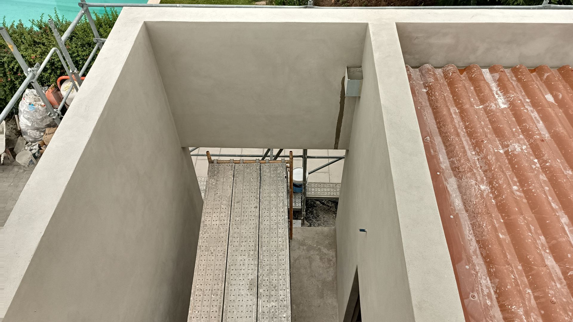 Vista aérea de um canteiro de obras com andaimes e um prédio com telhas laranja.