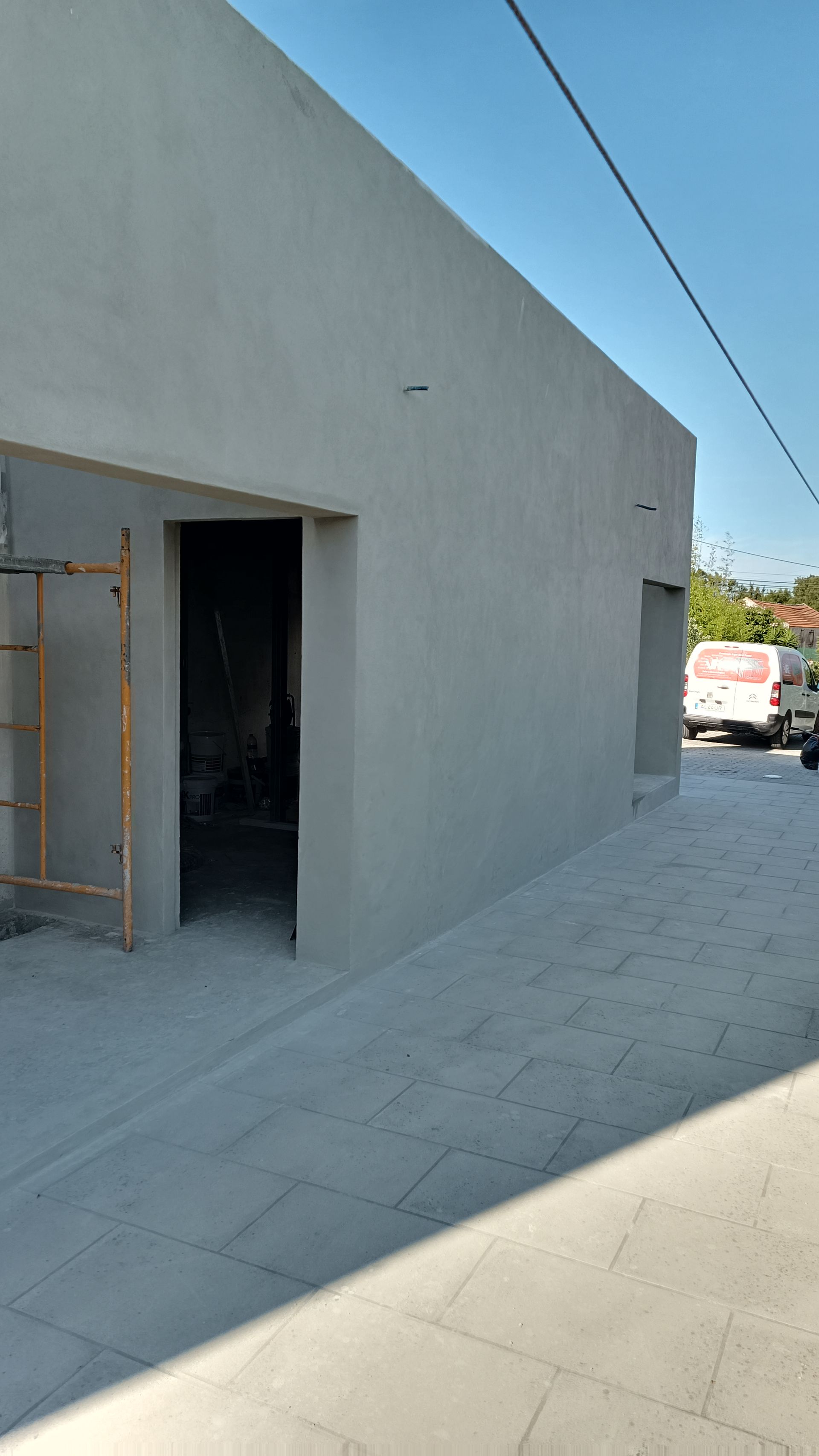 Prédio cinza com duas portas, escada e calçada pavimentada.