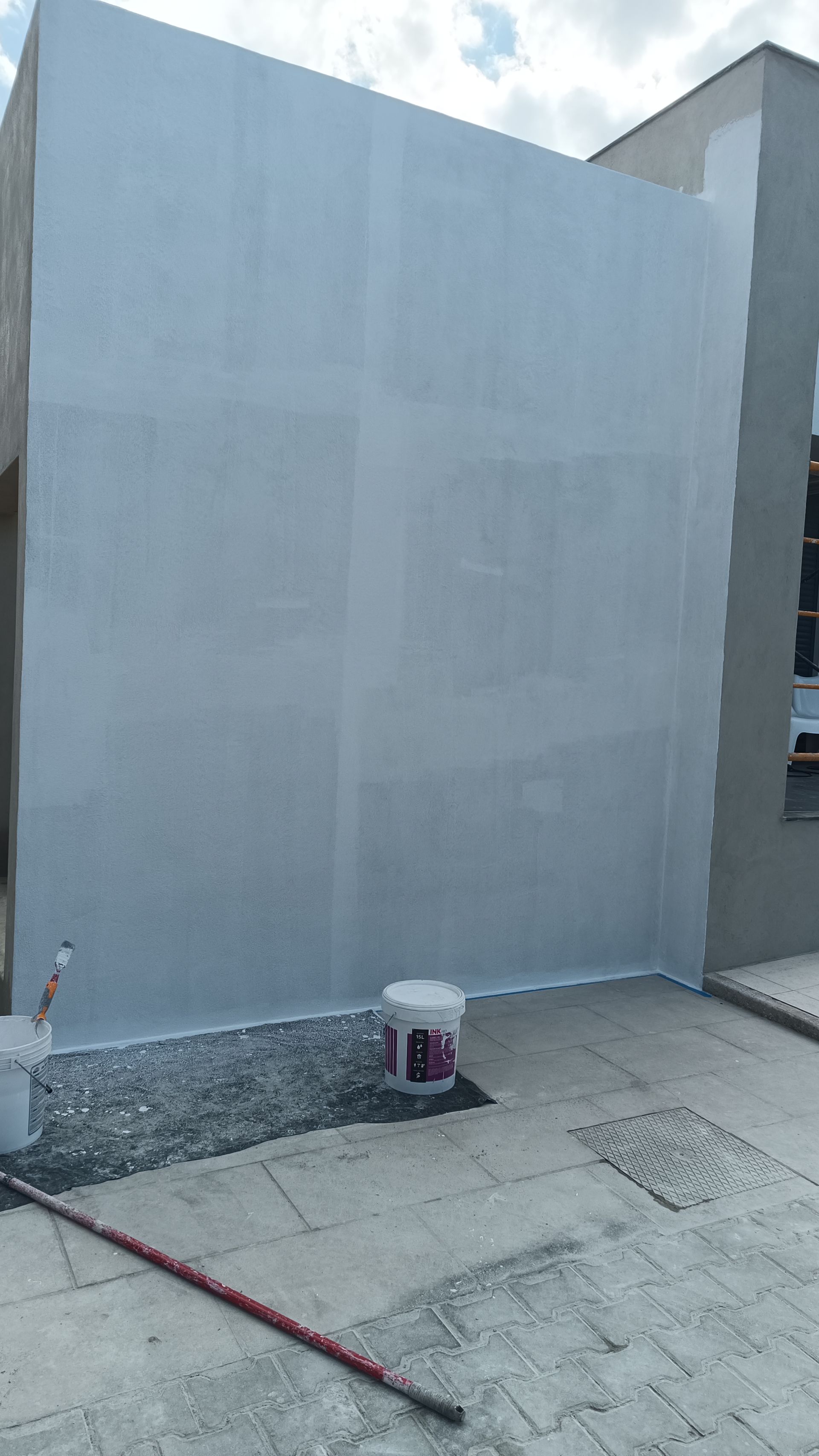 Parede externa recém-pintada de cinza, balde de tinta e cabo de rolo no chão.