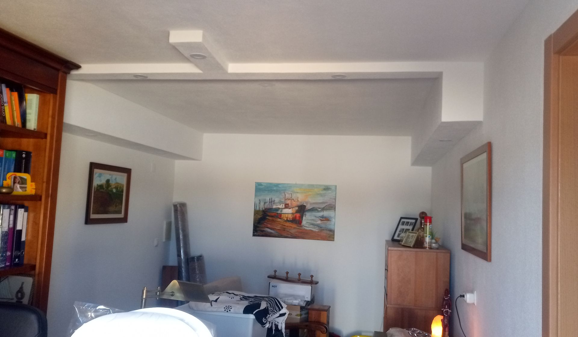 Sala de estar com estantes embutidas, obras de arte e uma estrutura de teto branca e angular.