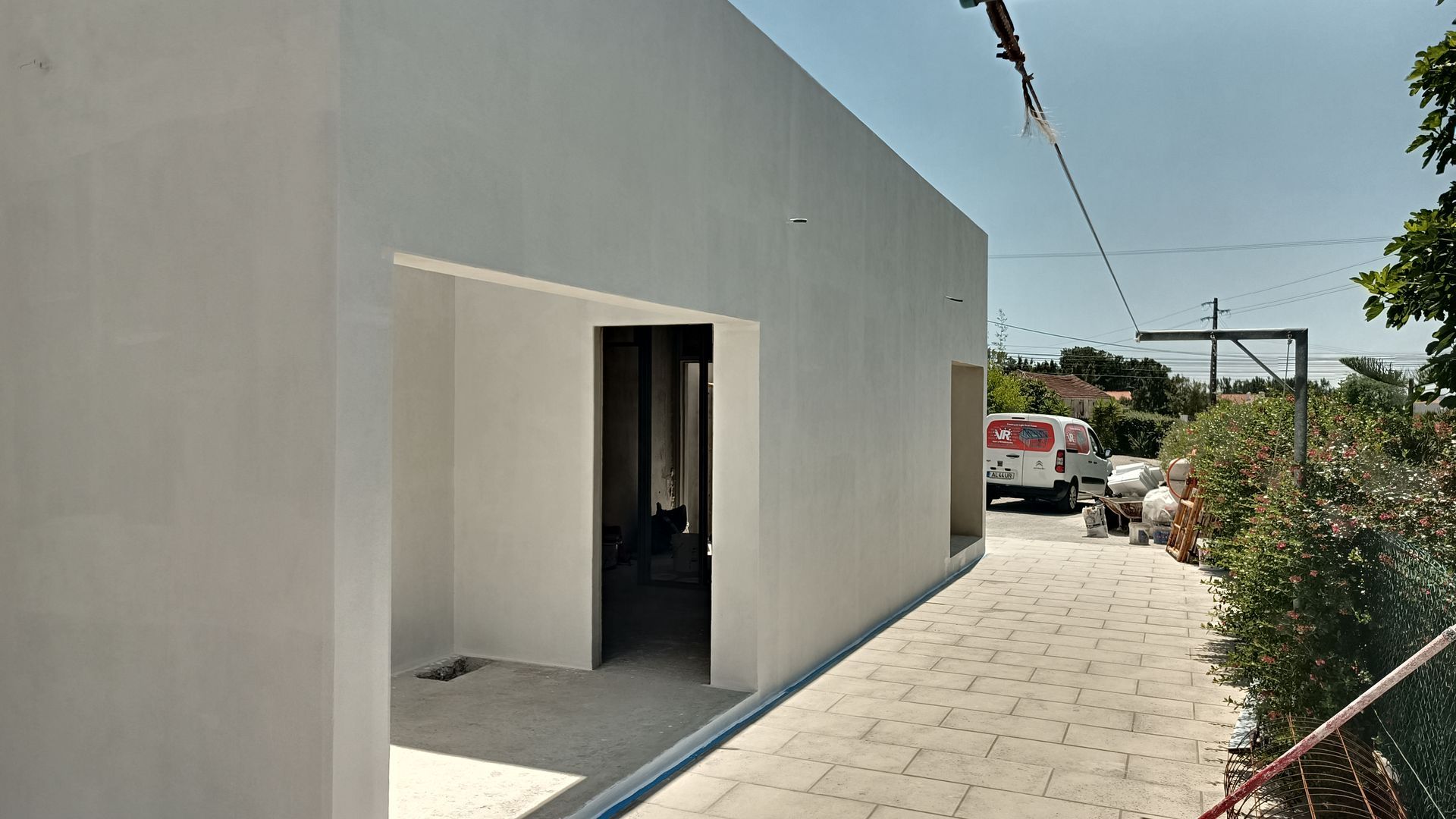 Prédio branco com porta aberta. Um caminho de tijolos leva ao prédio e uma van está estacionada nas proximidades.