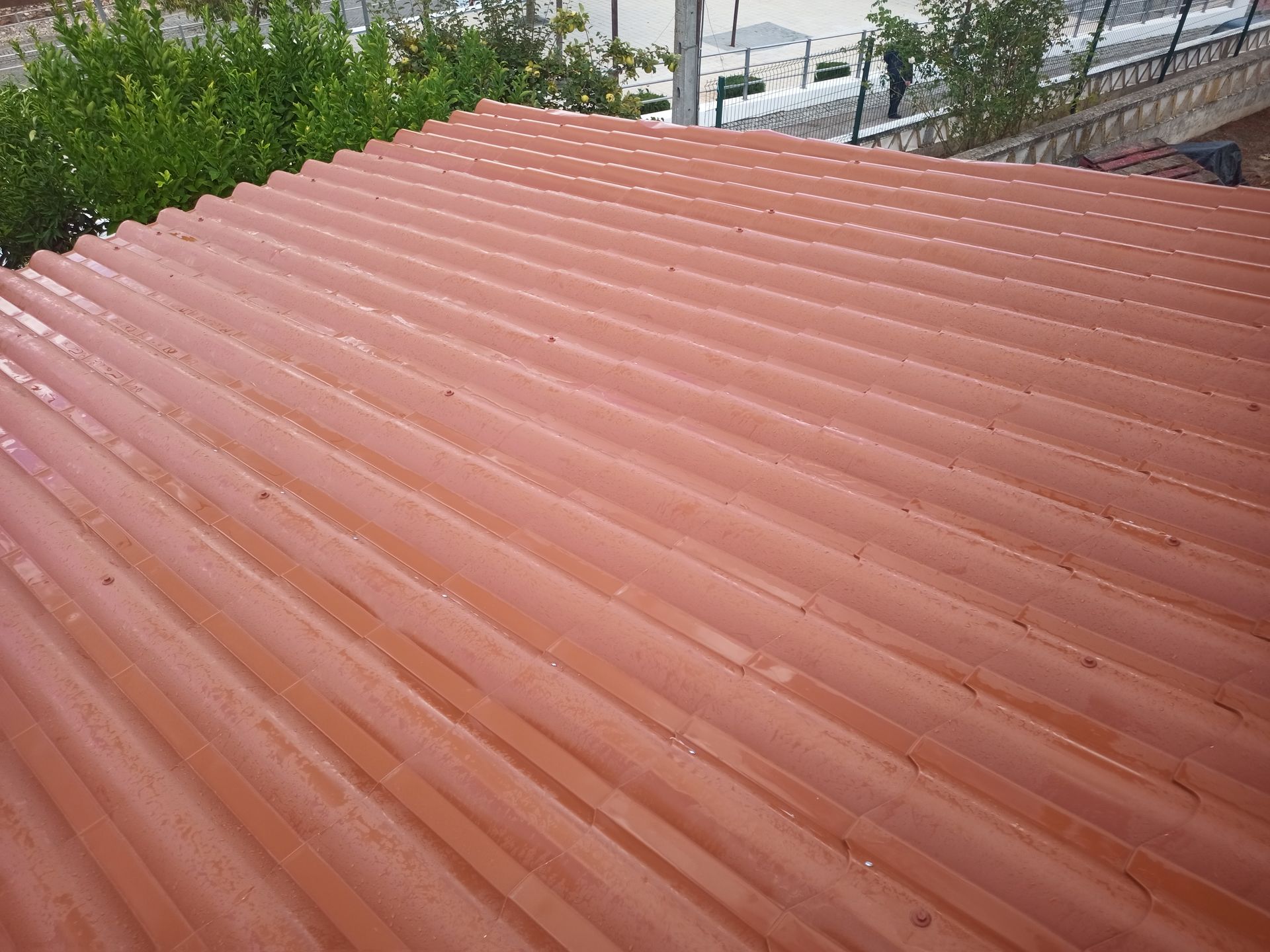 Telhado de zinco vermelho, provavelmente feito de barro ou telha, parcialmente úmido.