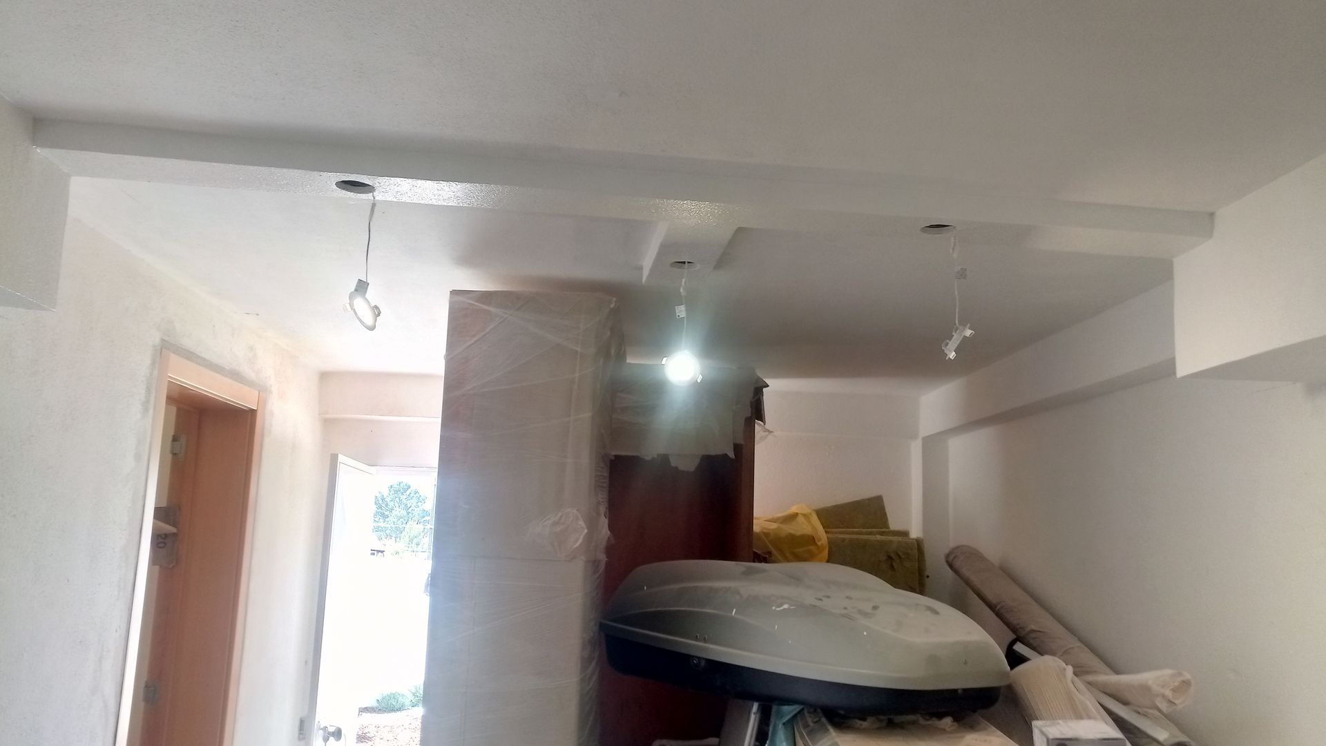 Interior de uma sala em construção com teto branco, fios expostos e entulho.