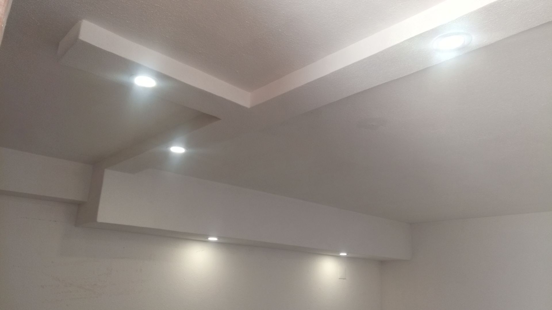 Teto rebaixado branco com várias luzes embutidas, projetando uma luz suave na parede abaixo.