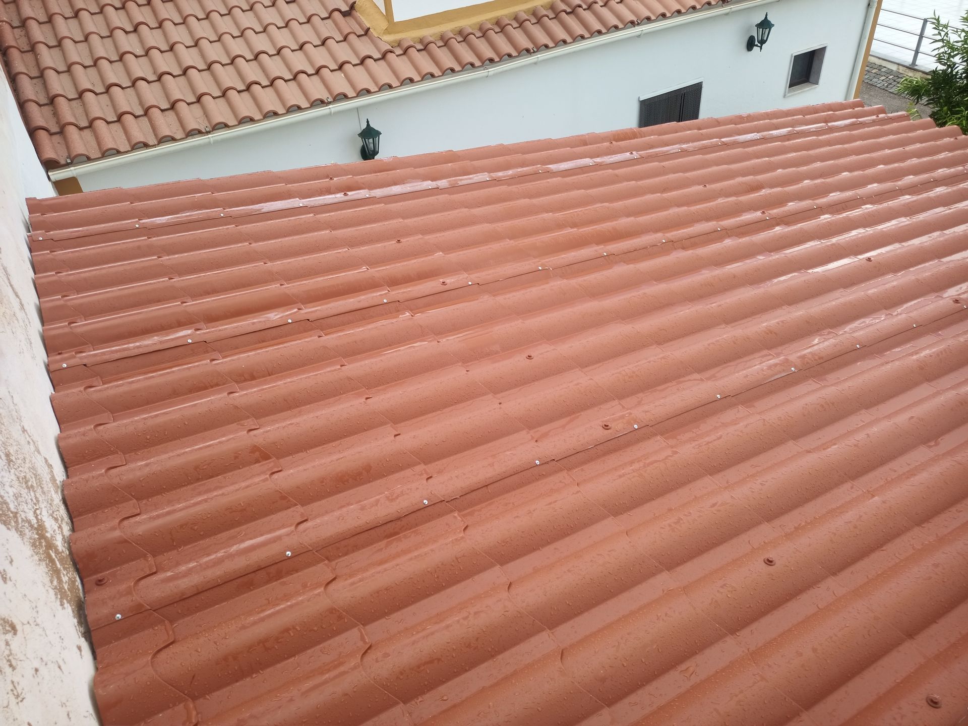 Telhado de telhas vermelhas onduladas, vista em ângulo do exterior do edifício, parcialmente ensolarado.