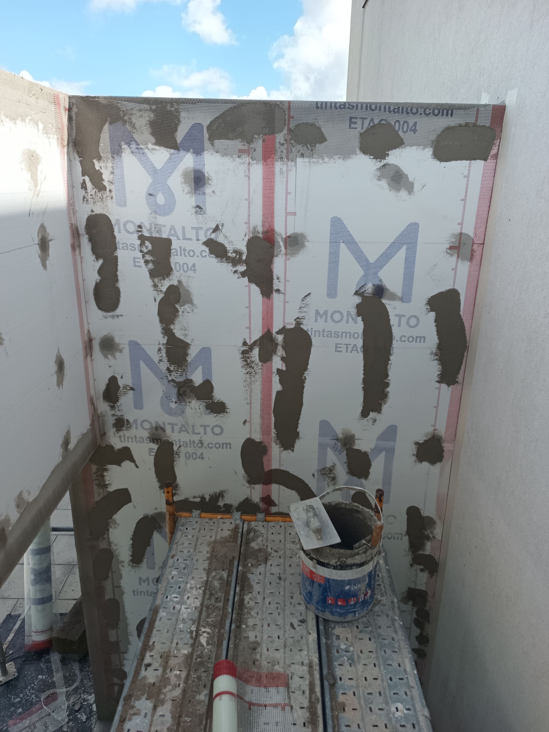 Construção de uma parede revestida com azulejos. Placas de isopor branco fixadas com argamassa na parede. Céu azul.