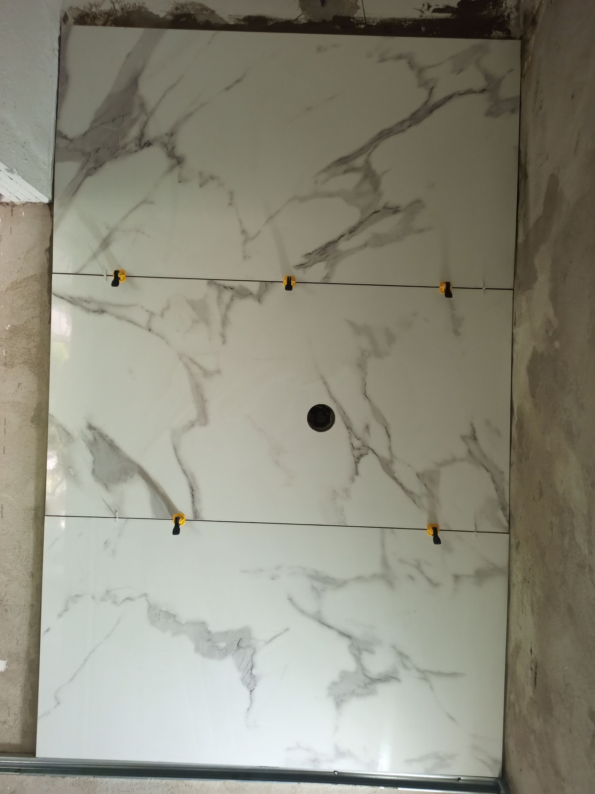 Azulejos de mármore branco com veios cinzentos foram instalados em uma parede, sendo visíveis os espaçadores amarelos.
