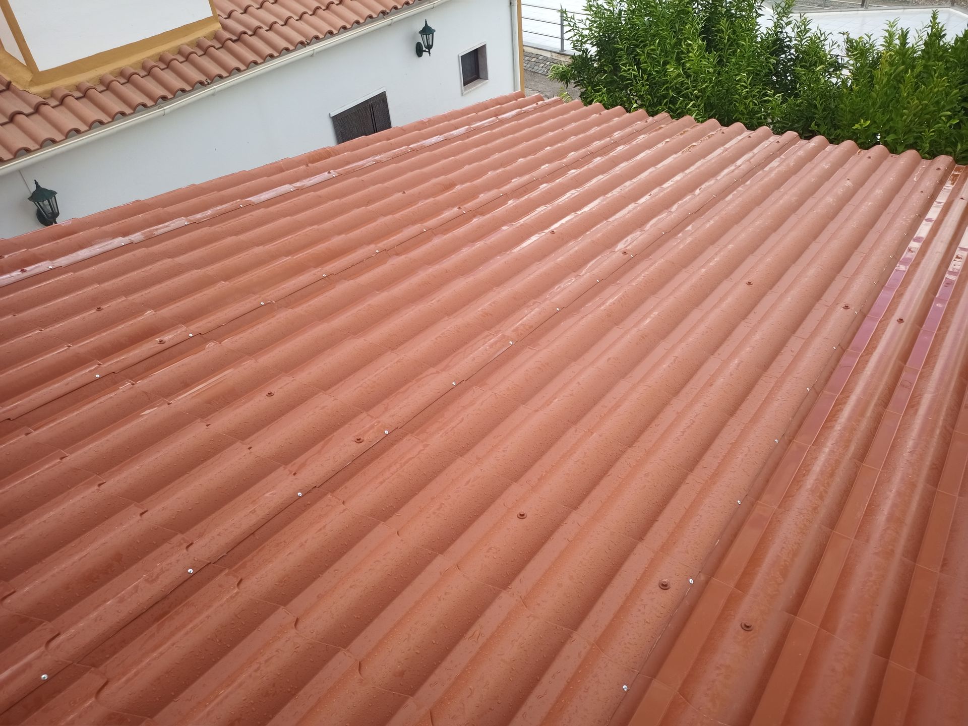 Telhado de zinco vermelho de um prédio com exterior branco e uma árvore ao fundo.