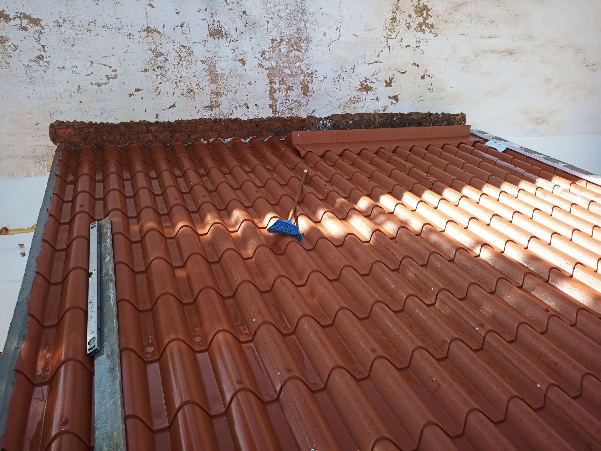 Telhado de telhas vermelhas com um objeto azul em cima, sob uma parede branca com tinta descascando.