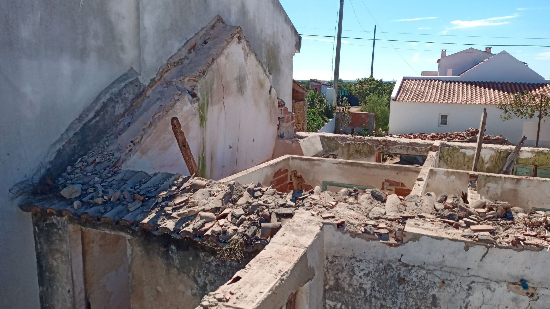Prédio demolido com entulho e vista das estruturas vizinhas em um dia ensolarado.