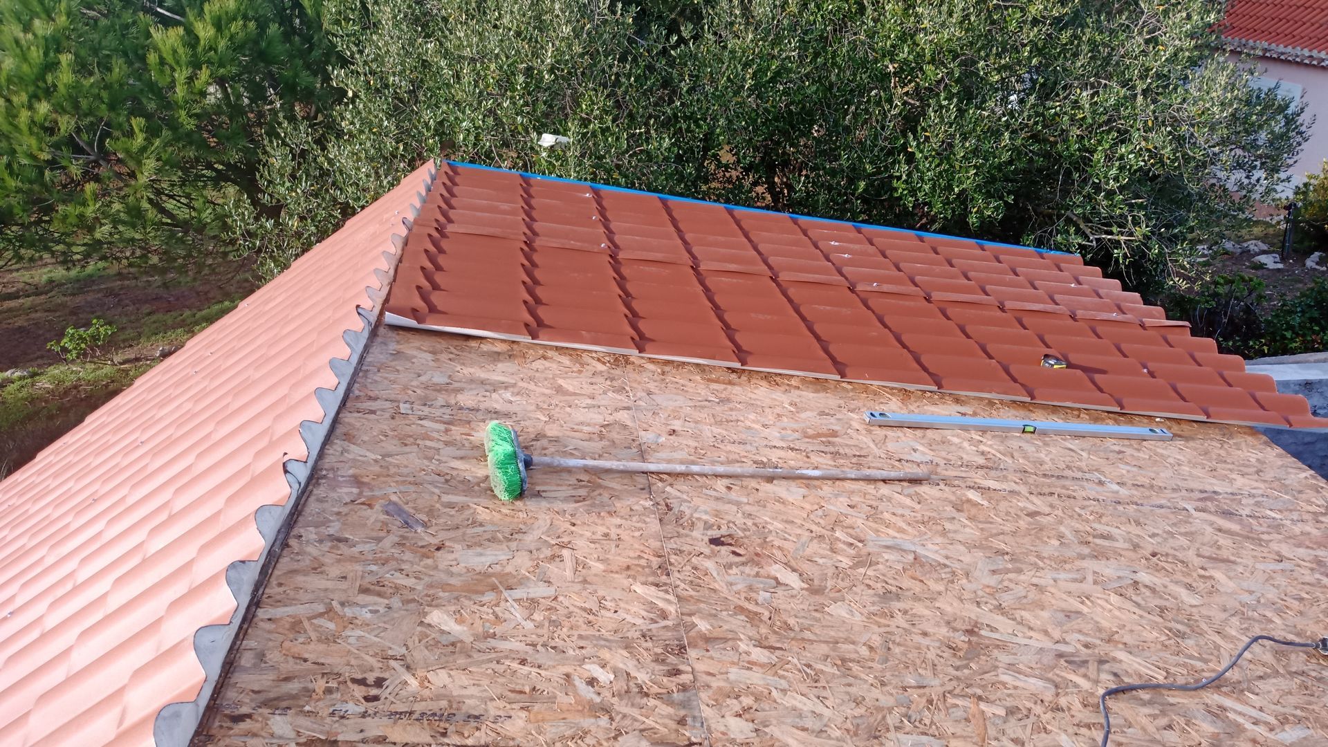 Telhado em construção, mostrando telhas de terracota parcialmente instaladas sobre madeira compensada.
