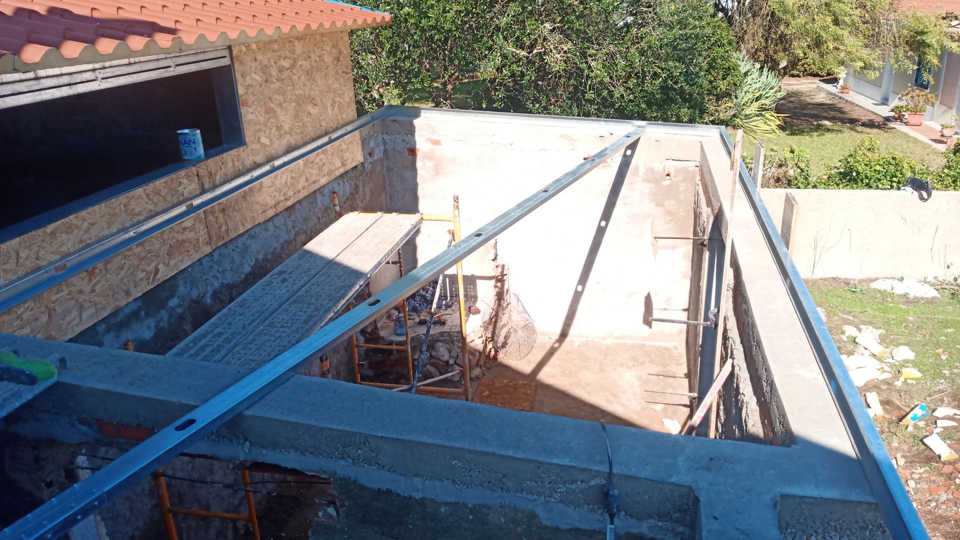 Canteiro de obras: estrutura de concreto com vigas aparentes e suportes metálicos. Ambiente externo, com luz natural.