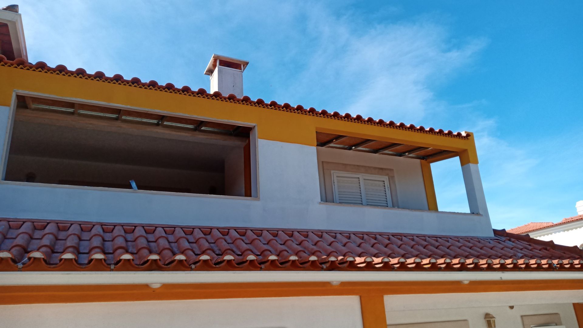 Casa de dois andares com fachada laranja e branca, telhado de terracota e céu azul.