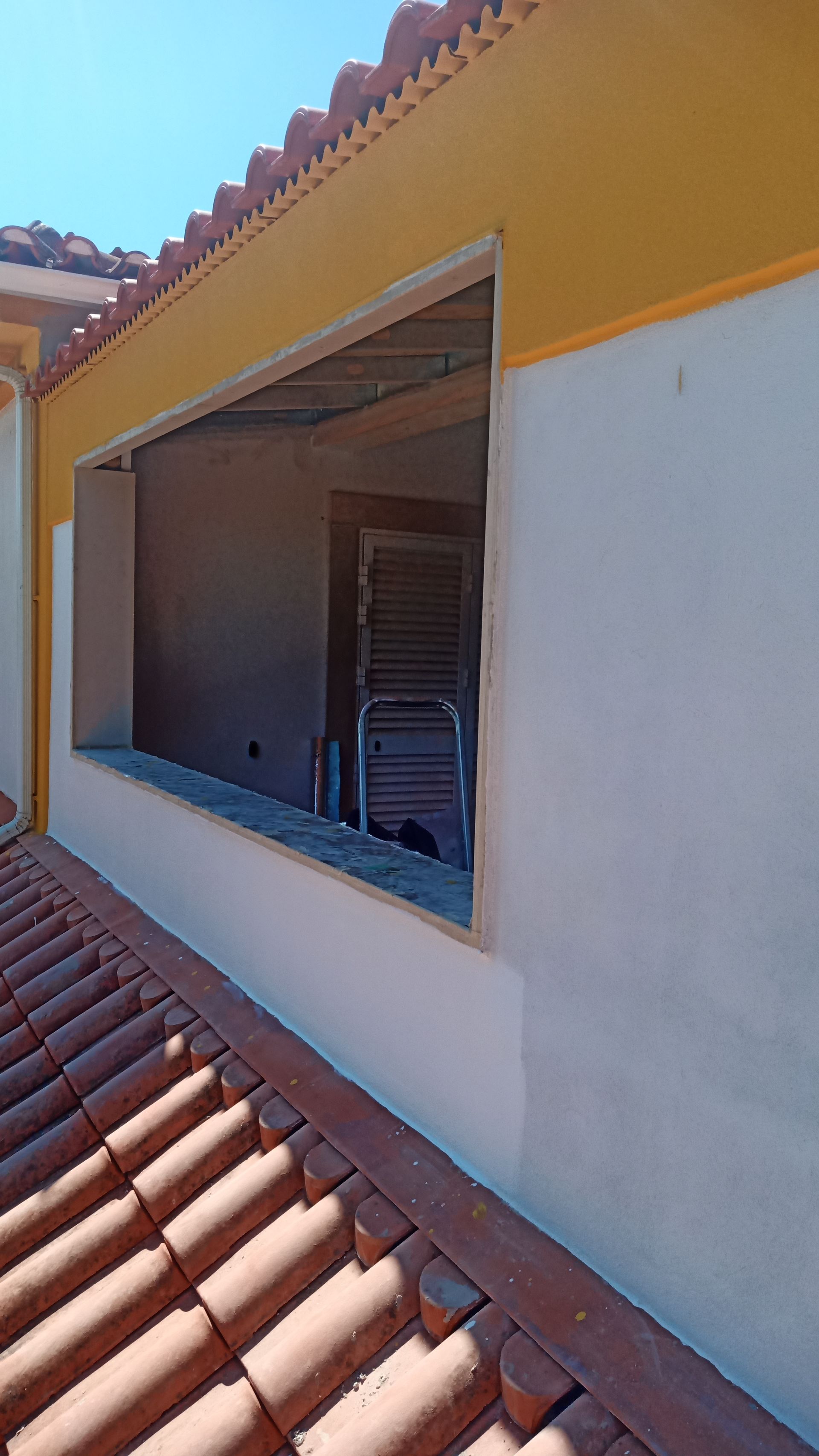 Vista exterior de um edifício com uma janela aberta; telhas vermelhas, paredes brancas e amarelas.