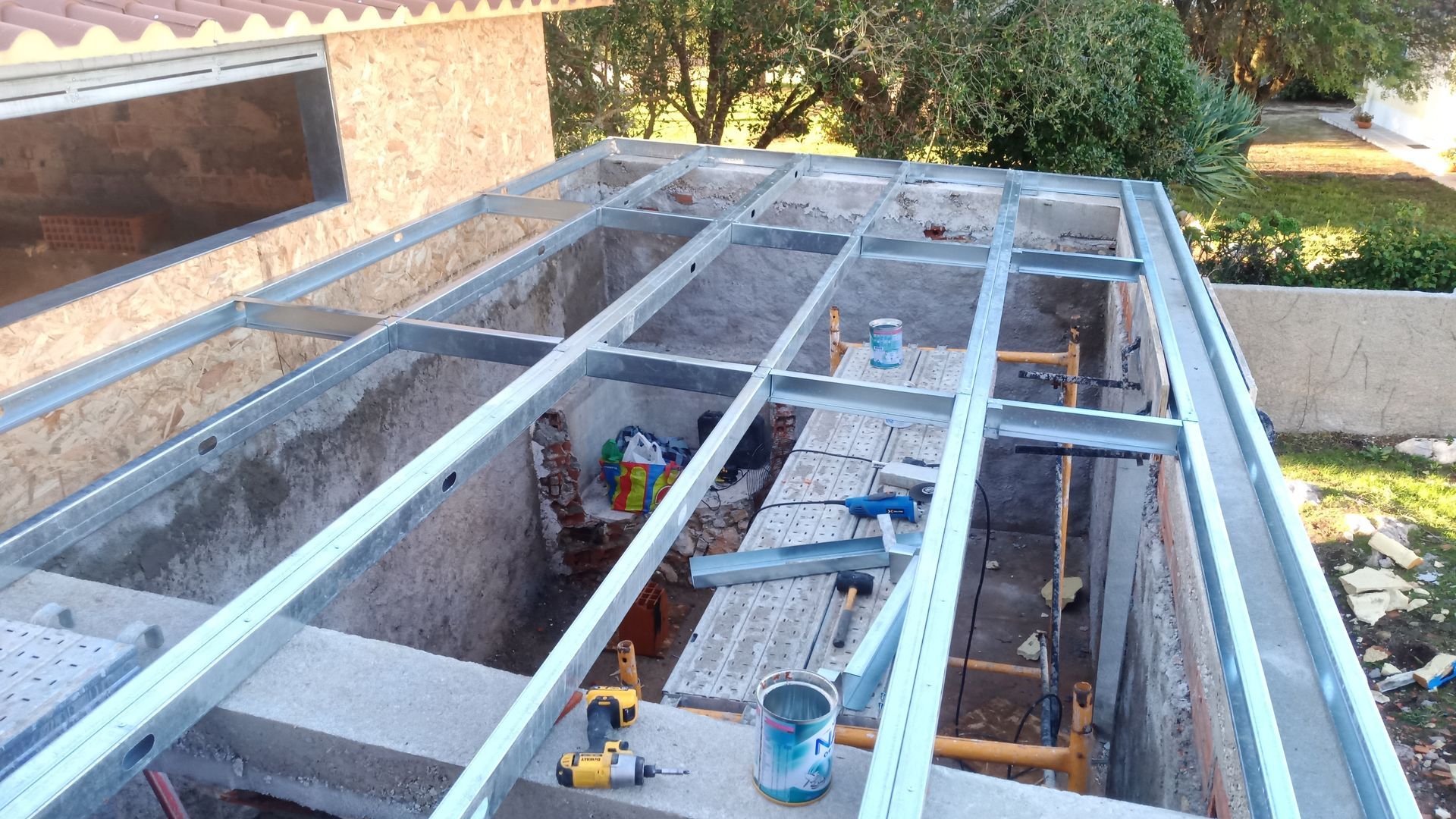 Construção de uma estrutura de cobertura metálica sobre uma base de concreto. Ferramentas e materiais são visíveis.