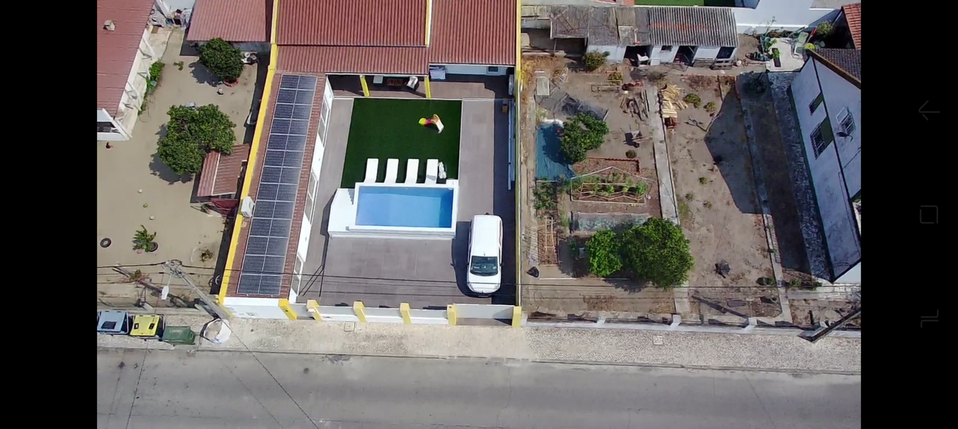 Vista aérea de uma propriedade com piscina, van, gramado verde e prédios ao longo de uma estrada.