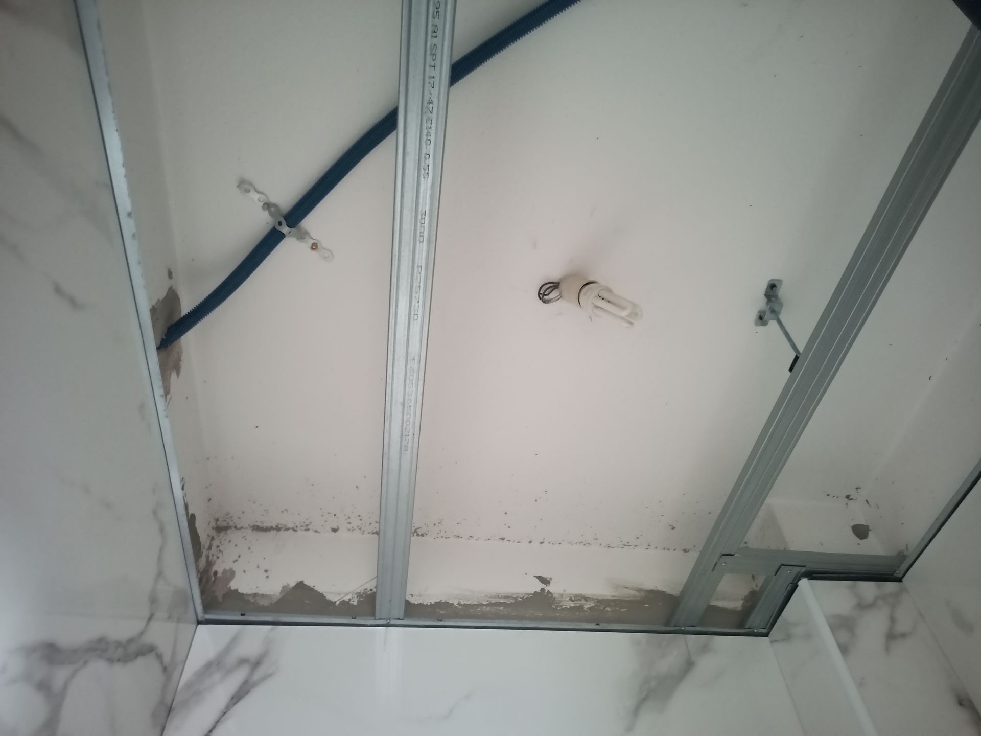 Teto em construção: estrutura metálica, fiação elétrica e drywall parcialmente instalado em um cômodo com piso de mármore.