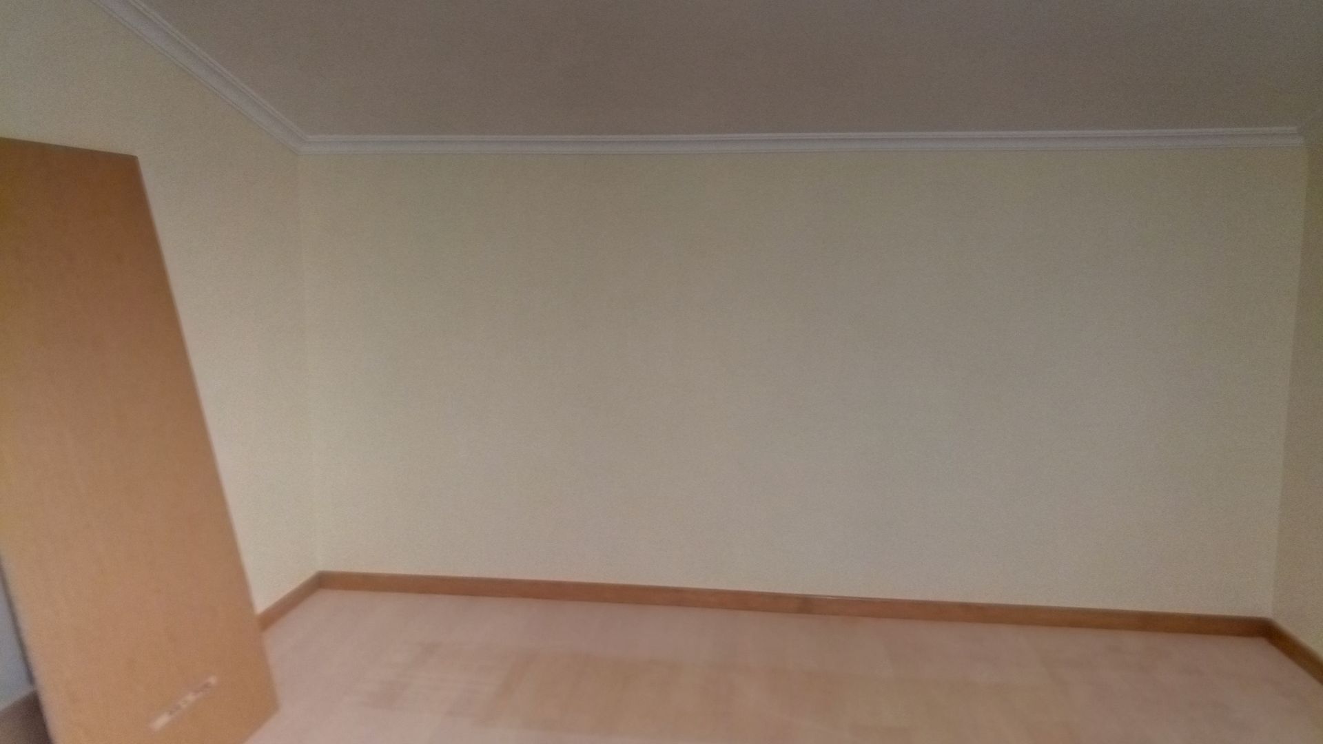 Quarto vazio com paredes amarelo-claras, piso de madeira e uma porta marrom encostada na parede.