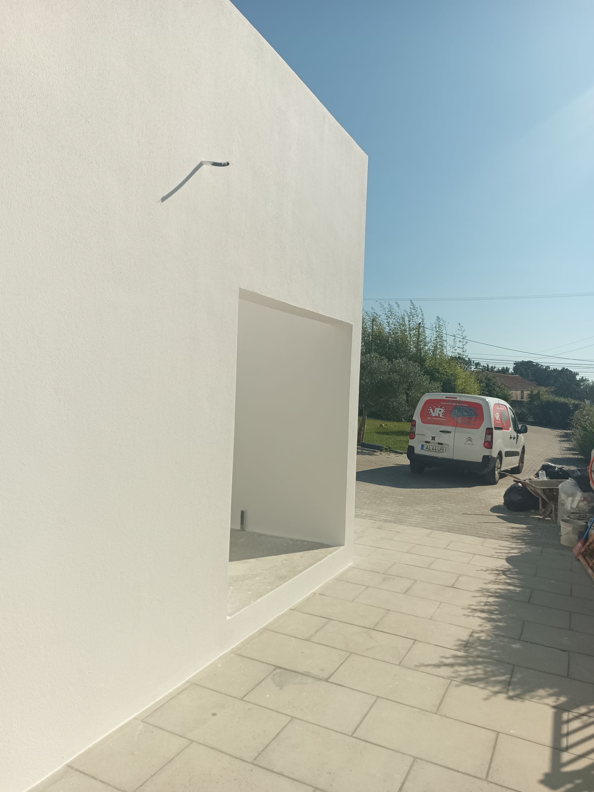 Exterior de um prédio branco com uma porta de entrada, caminho de pedra e uma van de serviço.