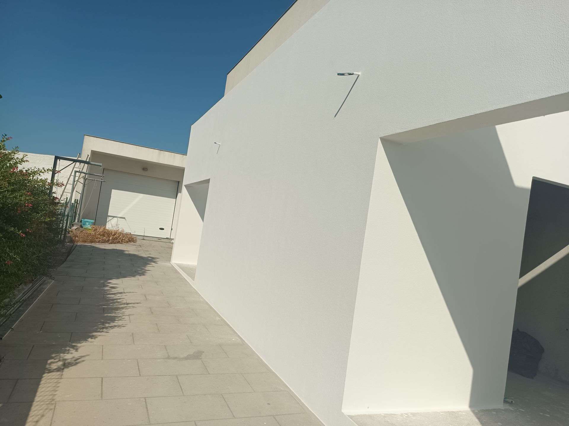 Exterior de edifício branco com aberturas angulares e passarela sob um céu azul claro.