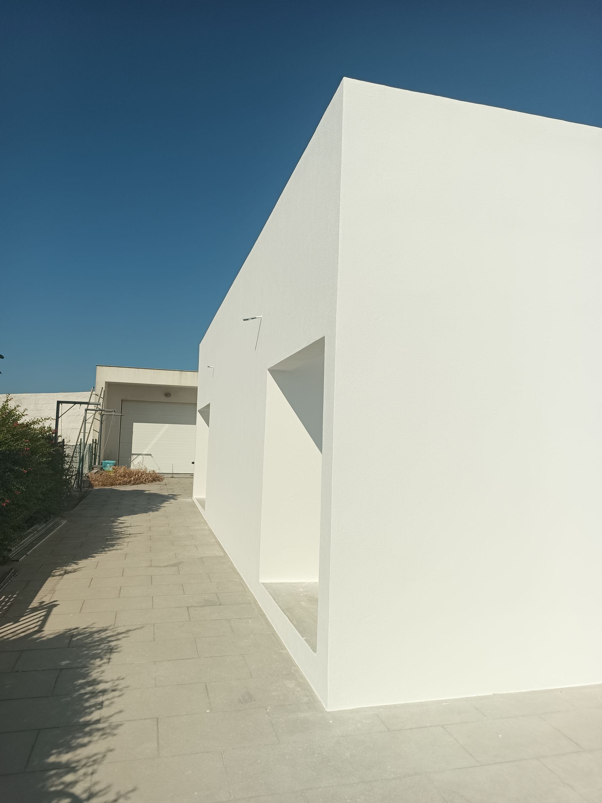 Prédio moderno branco com porta aberta, caminho de concreto e céu azul.