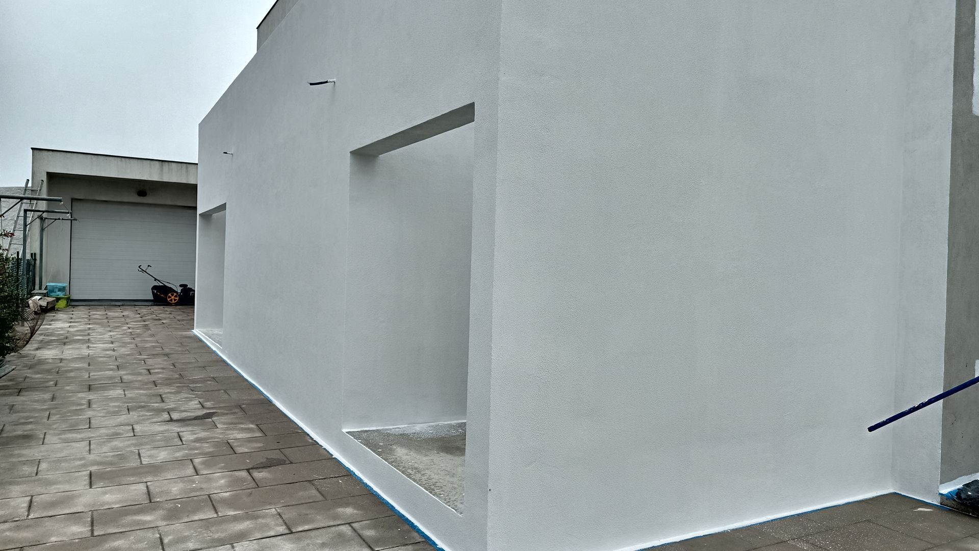 Paredes externas pintadas de branco de um prédio com uma passarela, detalhes em azul e céu nublado.