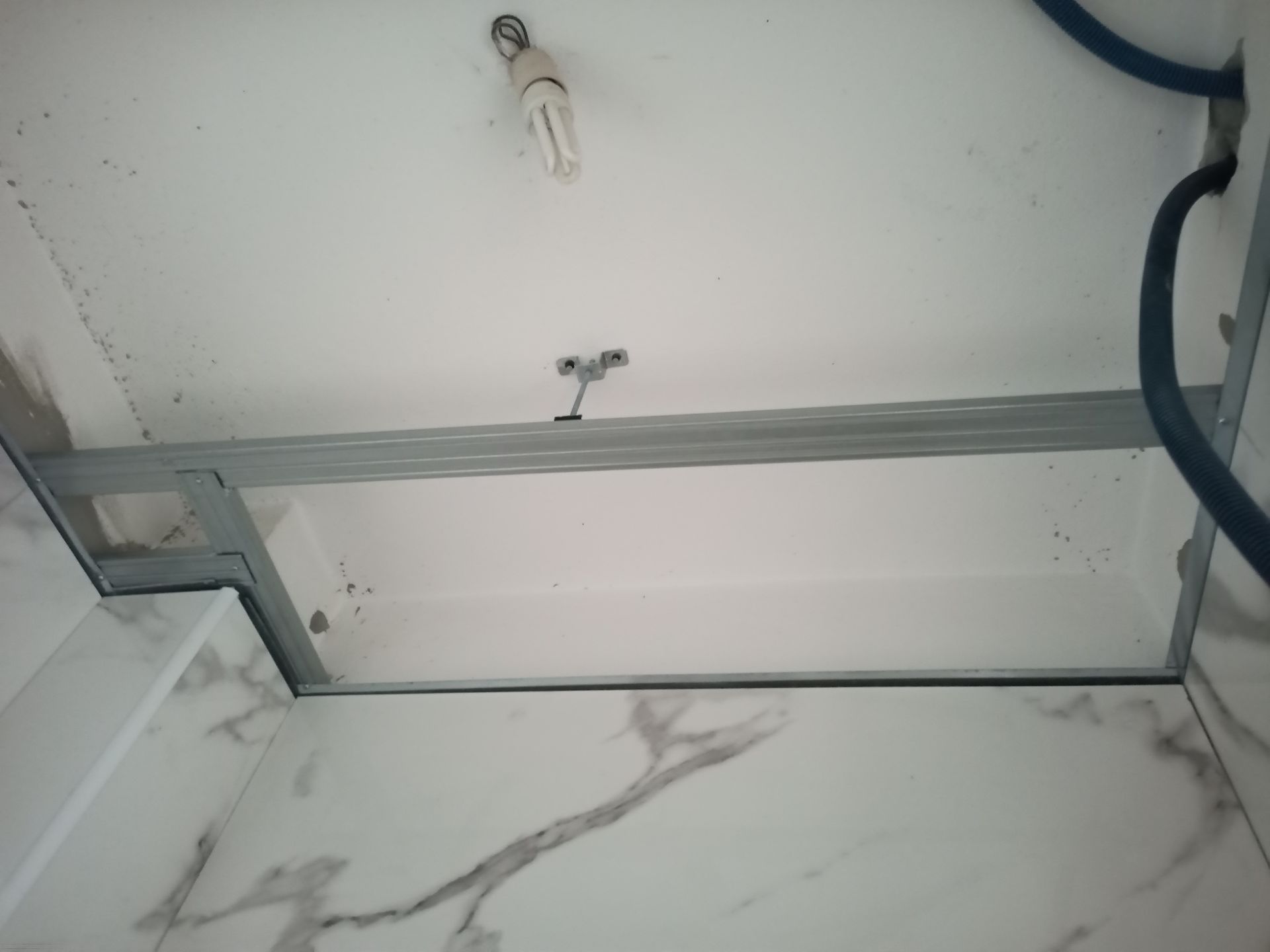 Estrutura metálica instalada em teto e parede brancos, com luminária e tubulação.