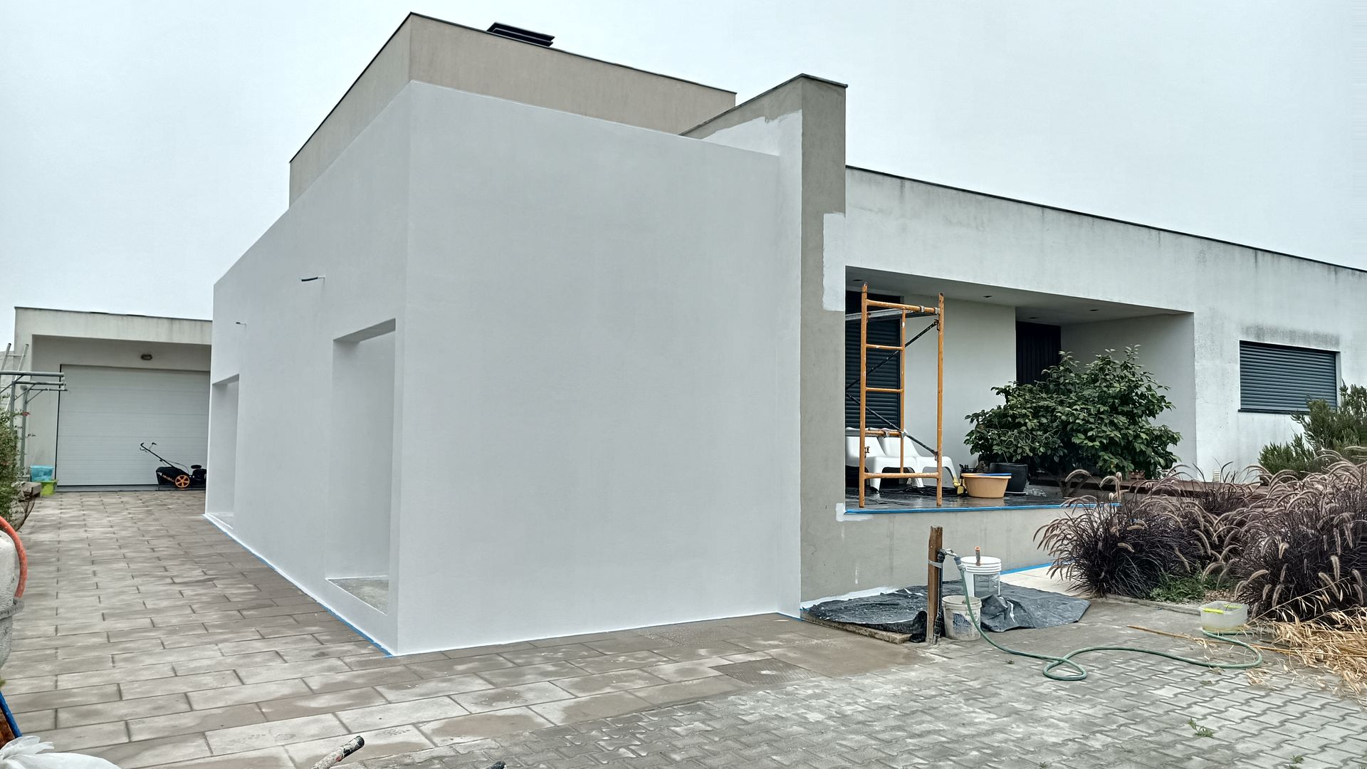 Casa moderna com paredes brancas e telhado cinza; materiais de construção expostos do lado de fora.