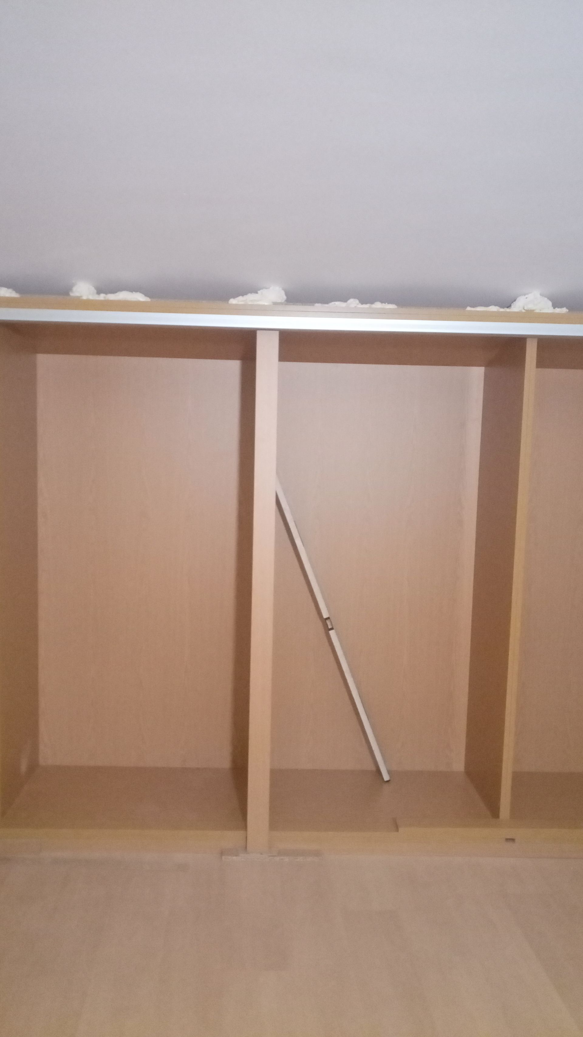 Armário embutido com três compartimentos; paredes bege, acabamento branco; um cano encostado no compartimento do meio.