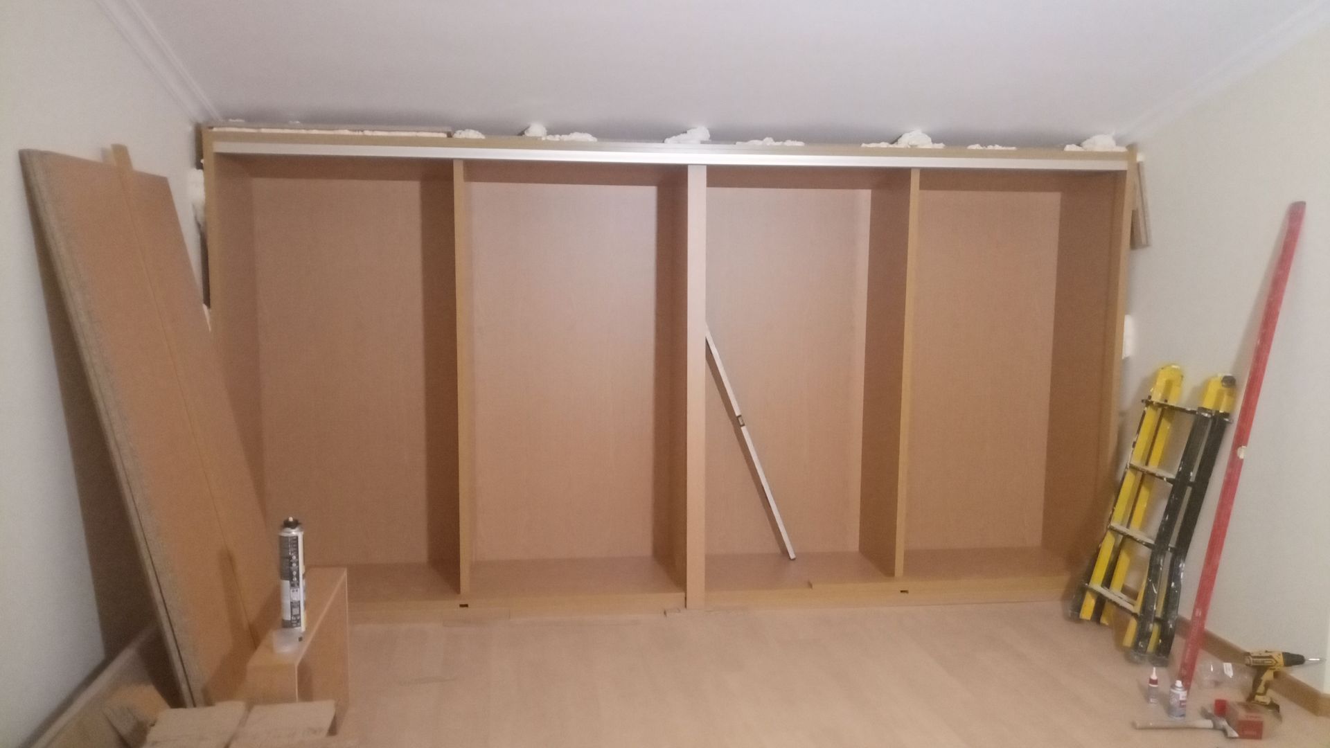 Um depósito parcialmente construído com quatro compartimentos marrons em um cômodo. Ferramentas e materiais estão próximos.