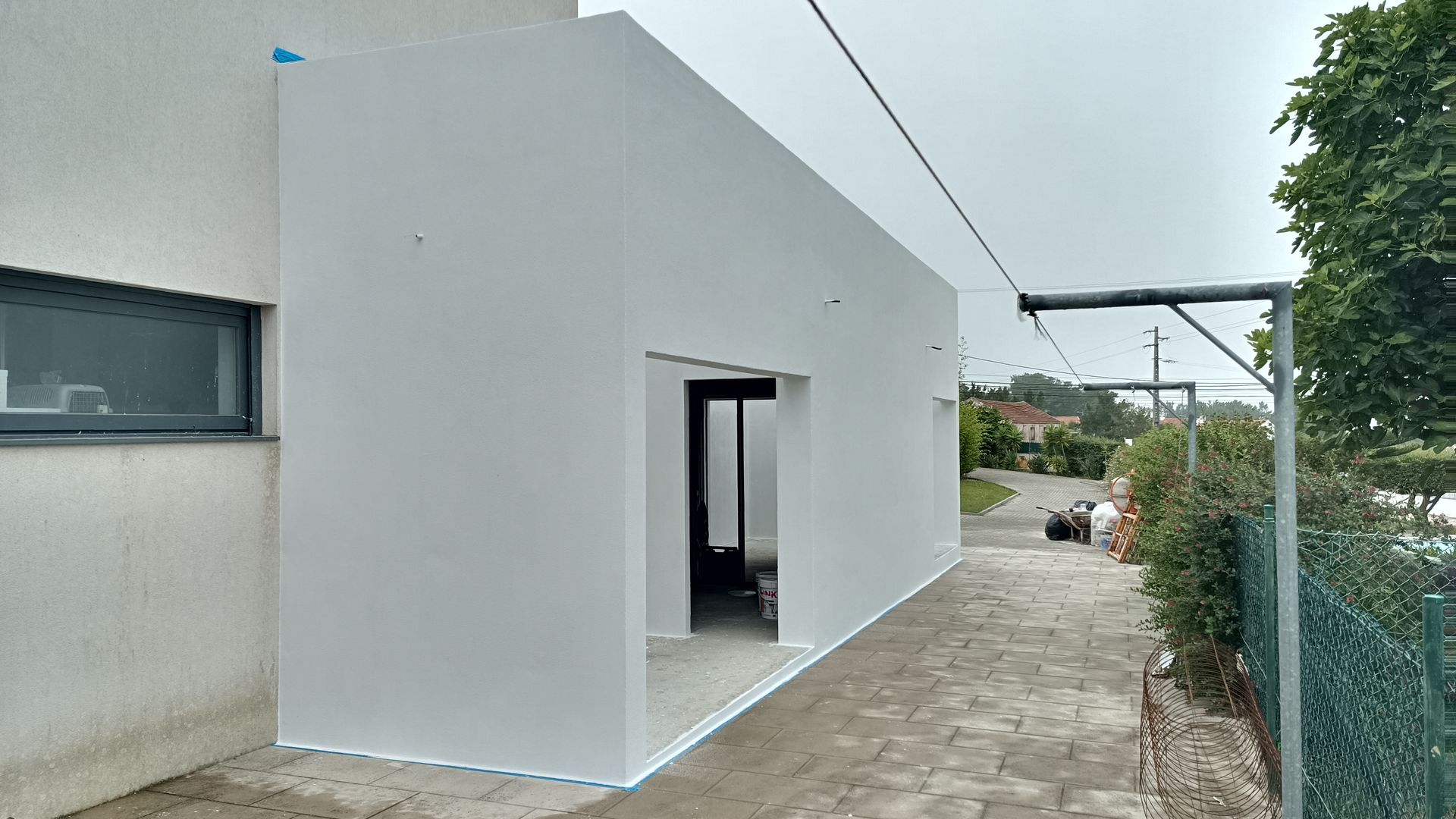 Anexo retangular branco ao lado de uma casa com janela de moldura escura.