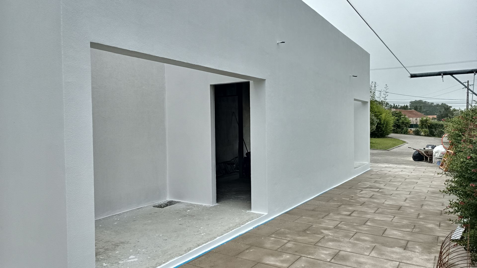 Fachada branca de um prédio com porta aberta. Calçada cinza em frente. Dia nublado.