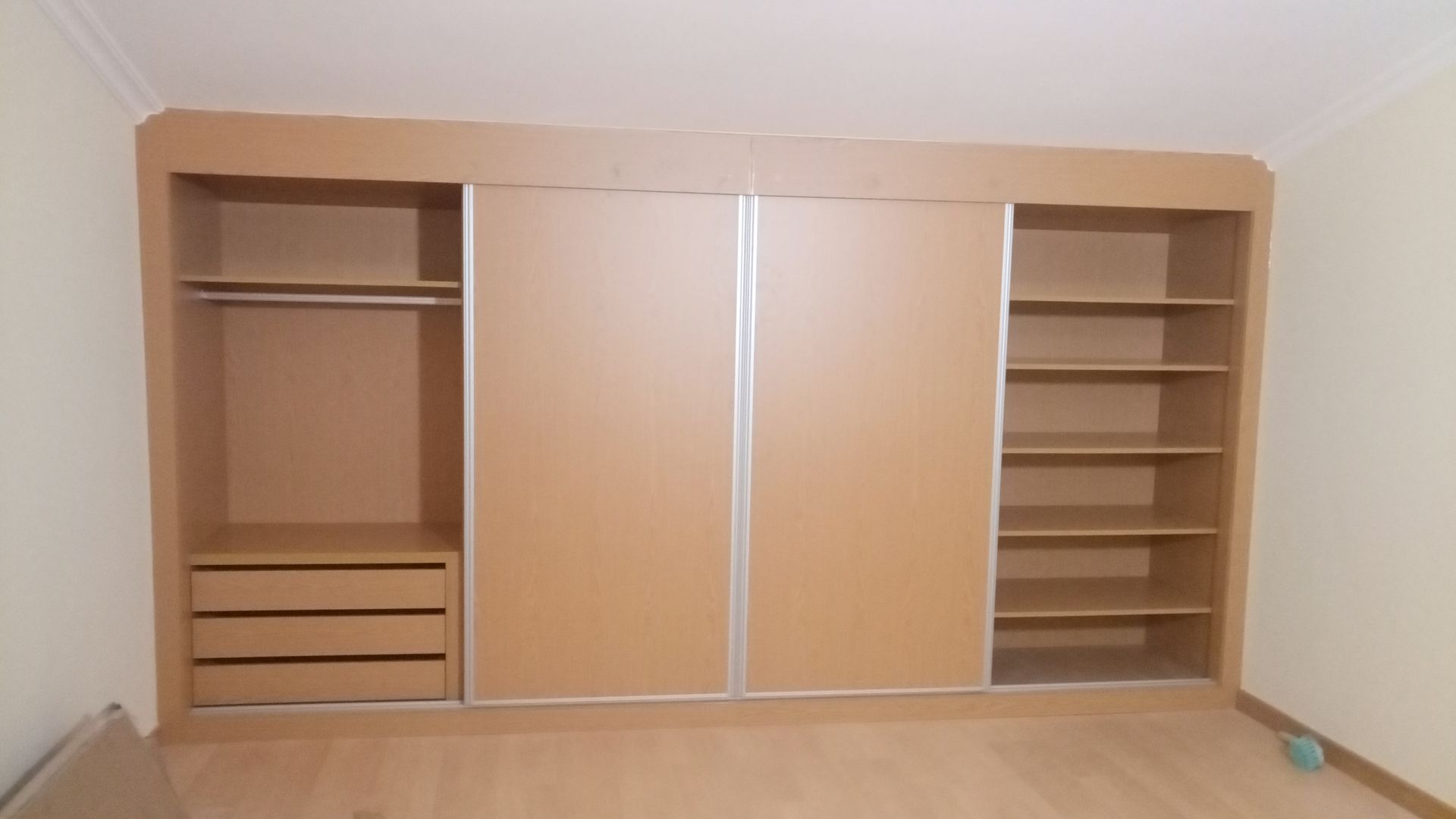 Armário embutido de madeira com portas de correr, varão para pendurar roupas, gavetas e prateleiras.