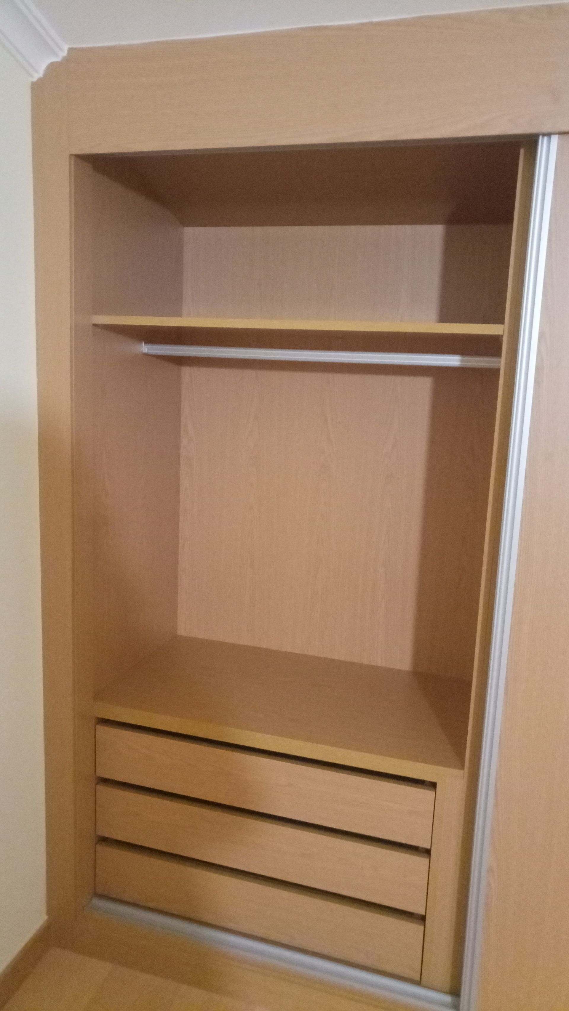 Armário embutido de madeira com porta de correr, prateleiras, varão para pendurar roupas e gavetas.