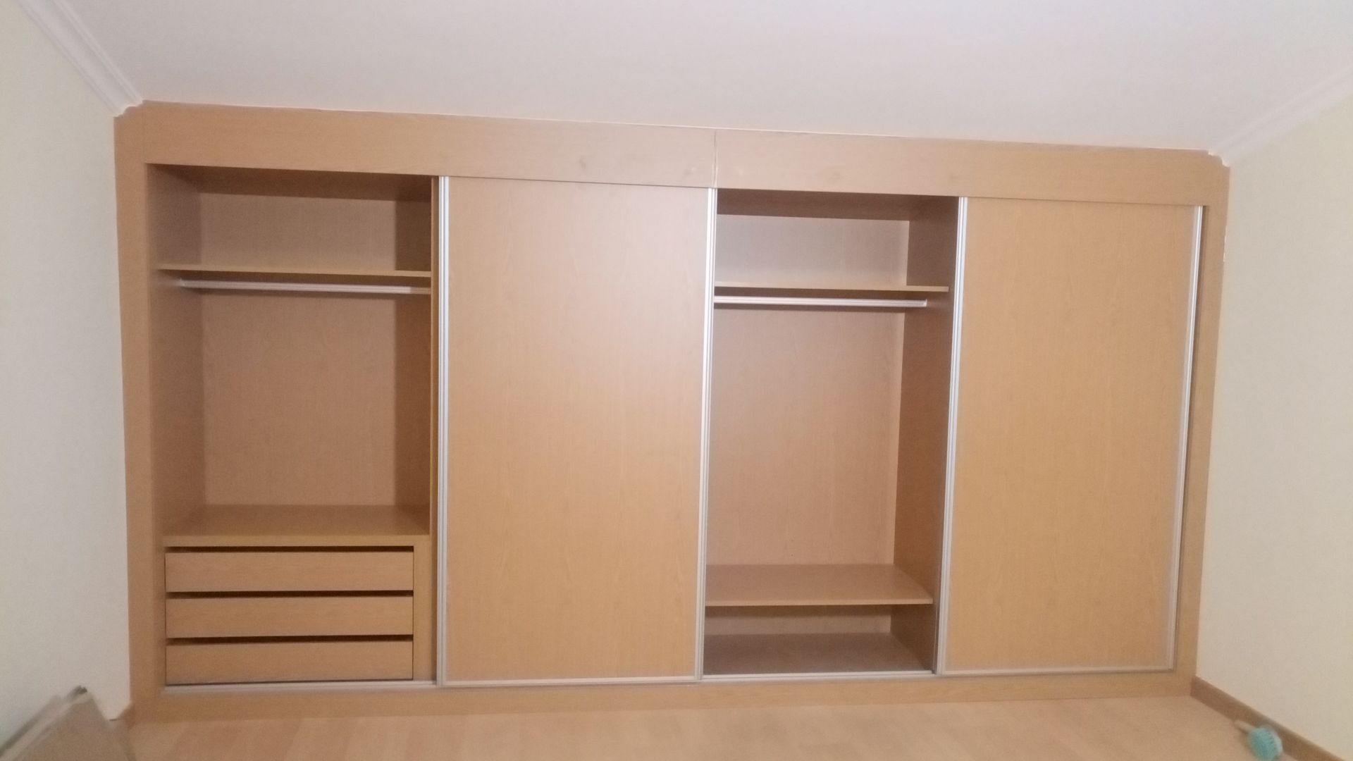 Armário de madeira com portas de correr e seções abertas que exibem prateleiras, gavetas e varões para pendurar roupas.