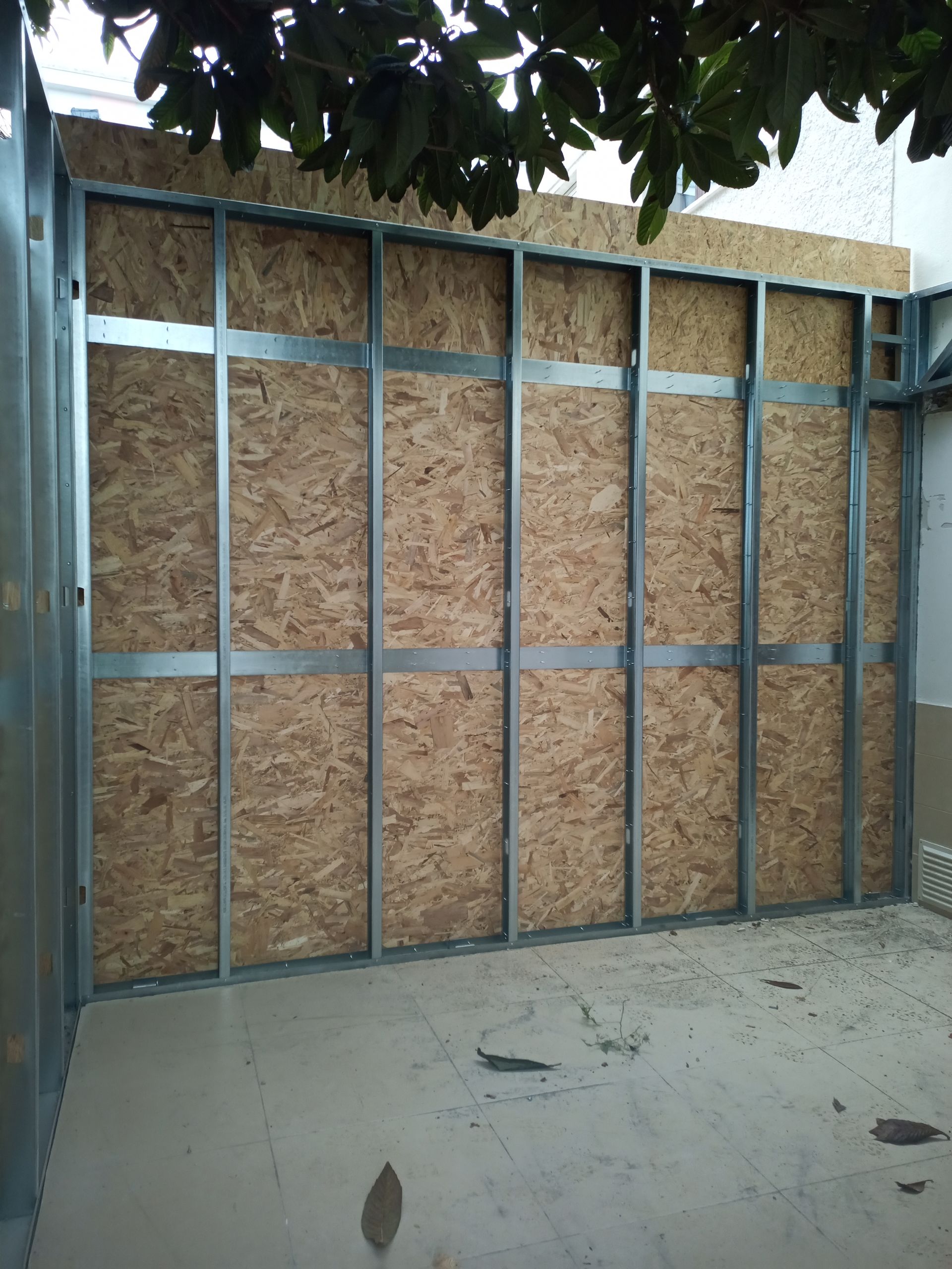 Estrutura de metal com painéis de madeira, parede parcialmente construída na área externa. Piso de concreto claro.