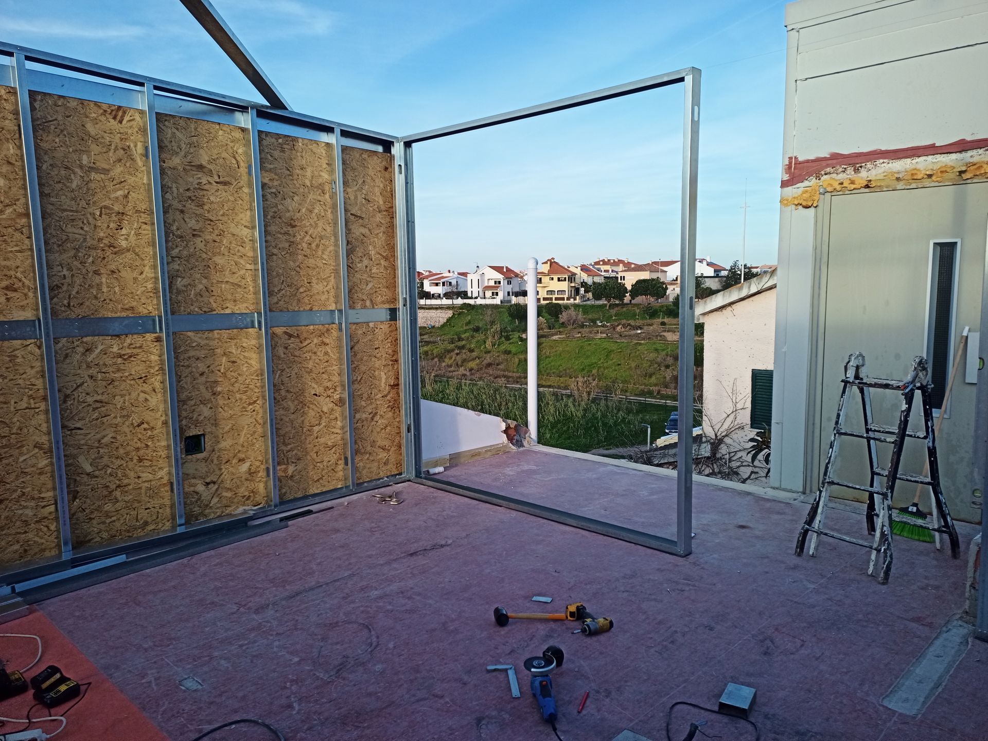 Estrutura interna: estrutura metálica com isolamento e vista externa para uma área residencial sob um céu azul.