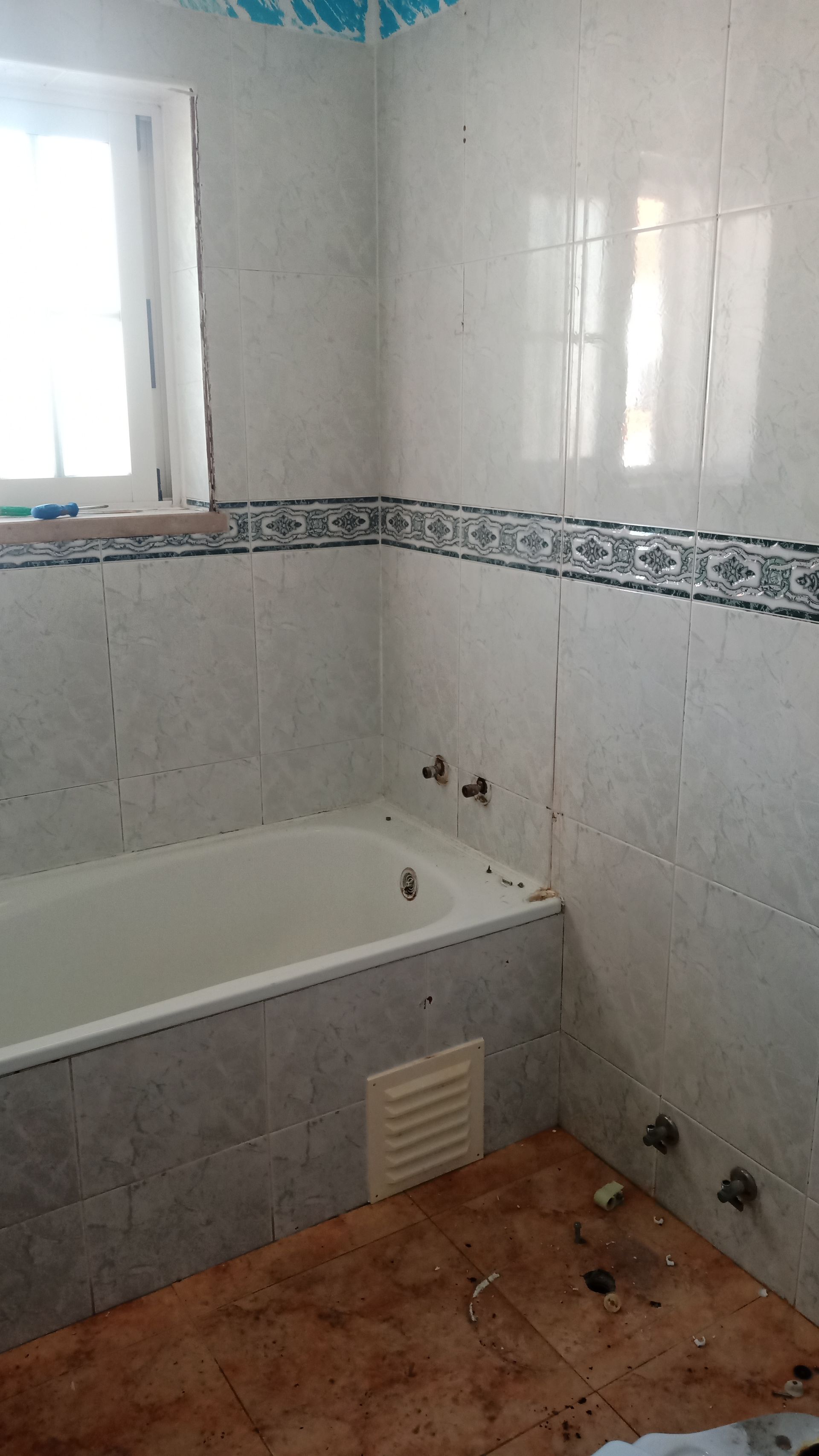 Banheiro com paredes revestidas de azulejos, banheira, janela e ventilação; o piso é parcialmente revestido com azulejos.