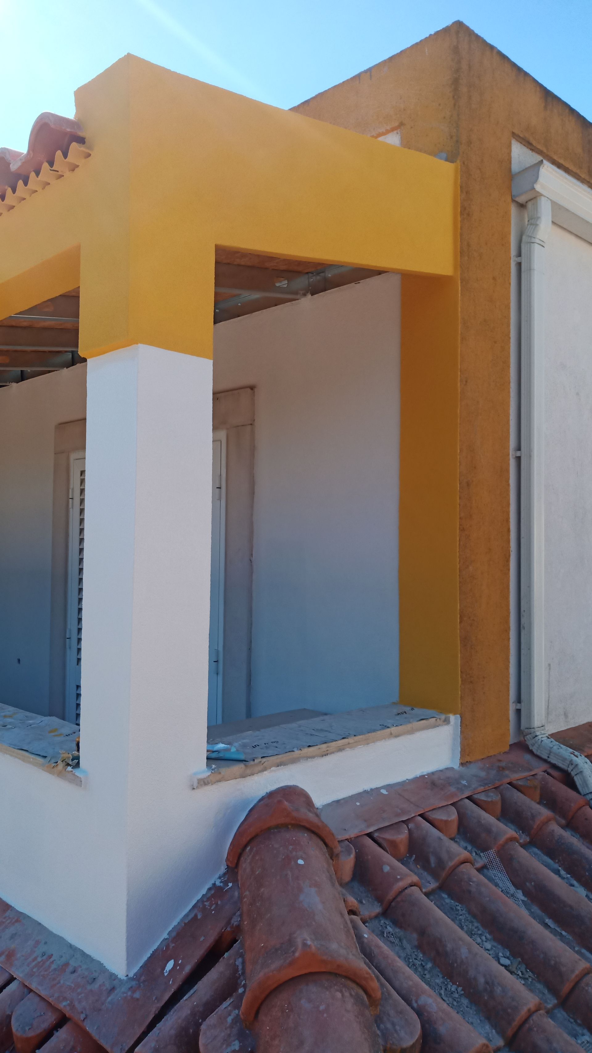 Esquina de prédio pintada de amarelo e branco, telhas de terracota.
