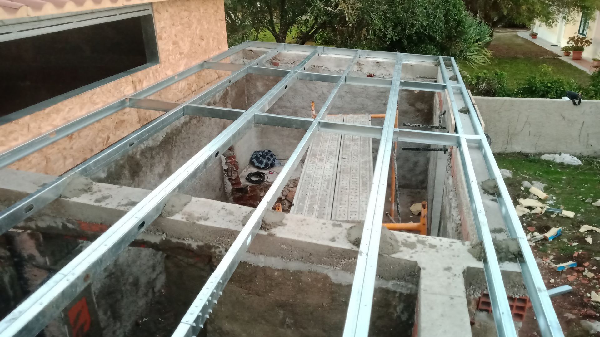 Estrutura metálica sobre blocos de concreto, provavelmente para uma extensão de telhado, em ambiente externo.