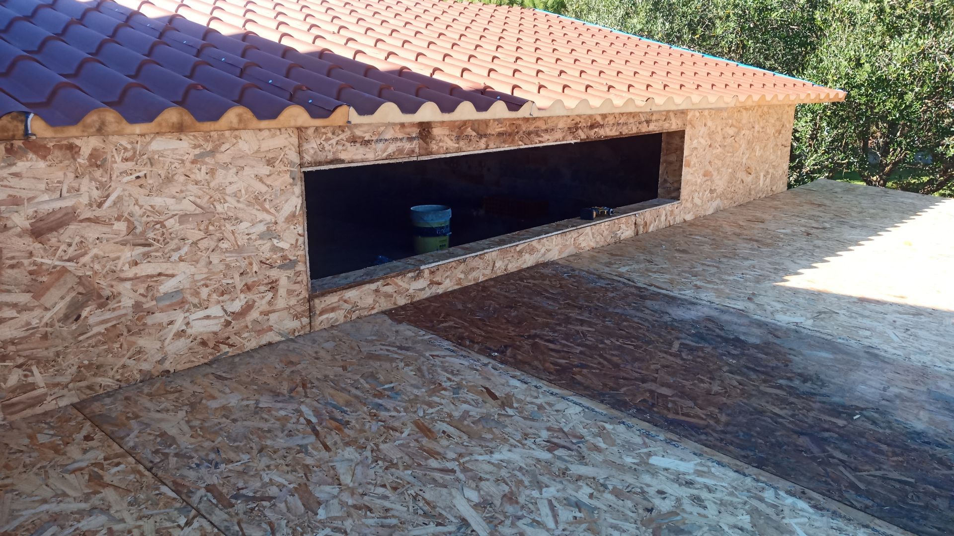 Uma pequena estrutura de madeira com telhado de telhas vermelhas e um espaço retangular aberto.