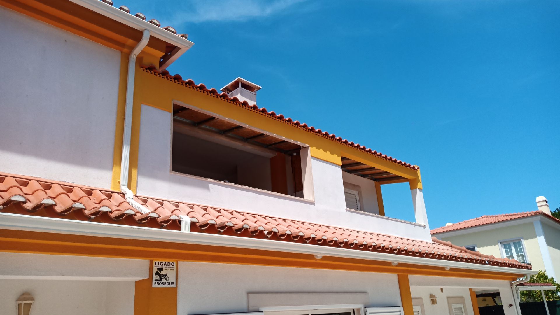 Prédio branco de dois andares com detalhes em laranja e telhas no telhado, contra um céu azul claro.