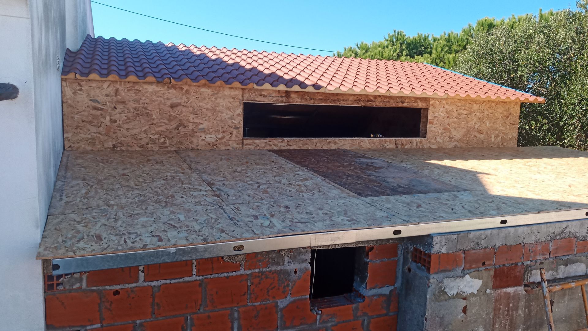 Construção de uma estrutura de telhado com OSB e telhas vermelhas, tendo como pano de fundo um céu azul.
