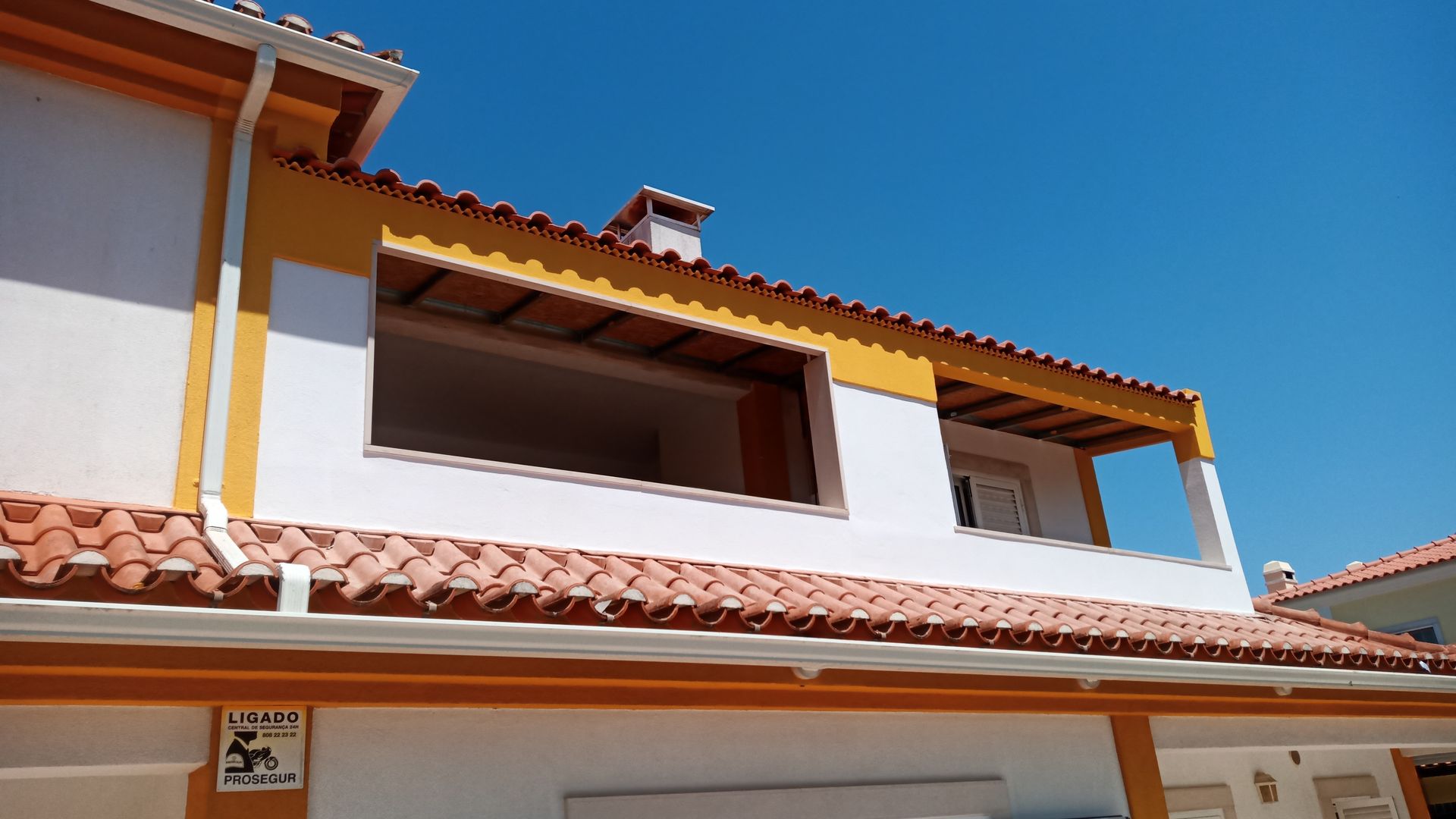 Prédio com telhas laranja, paredes brancas e detalhes em amarelo contra um céu azul.