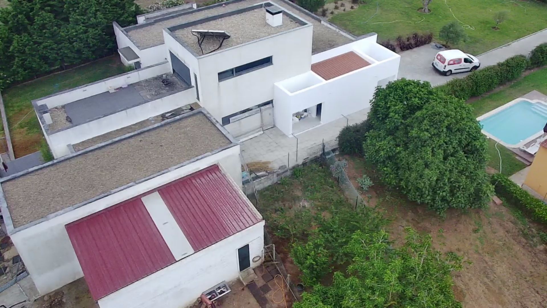 Casa moderna branca com telhados planos, piscina e anexo com telhado vermelho, vista de cima.