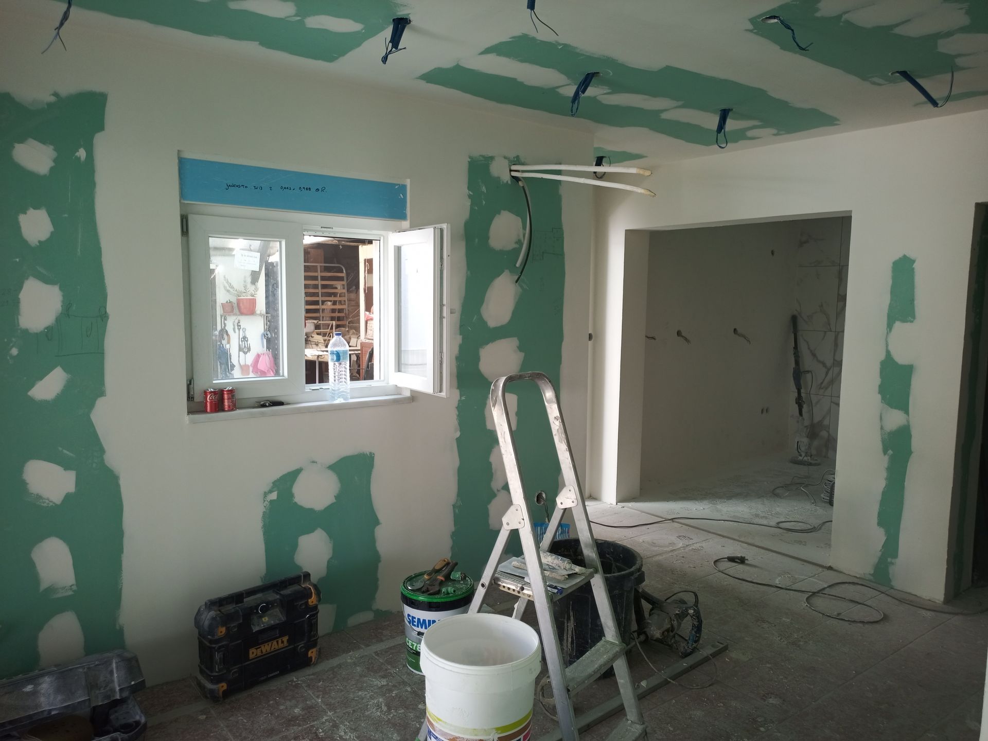 Quarto interior em reforma; drywall verde e massa corrida nas paredes, escada, janela.
