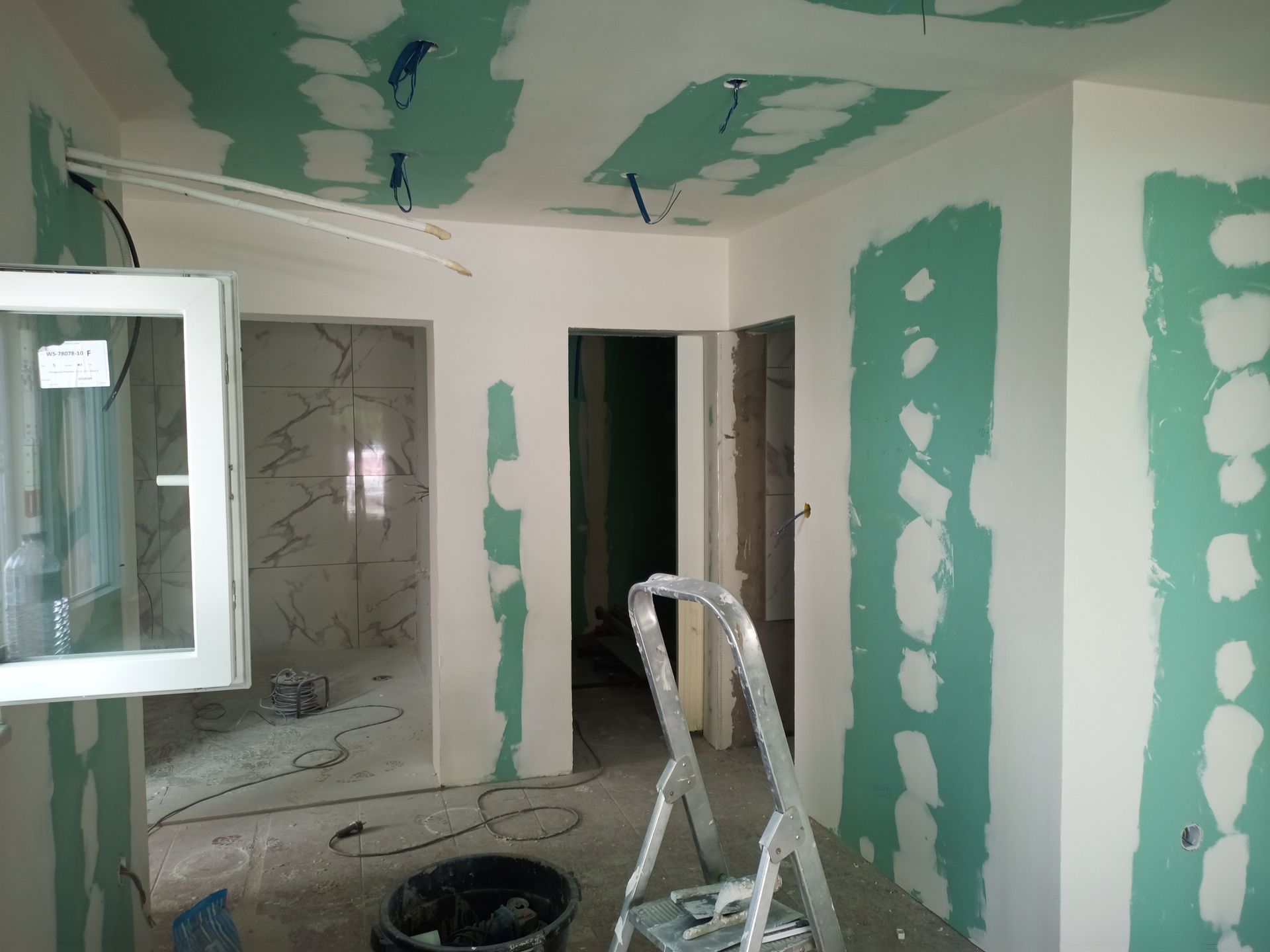 Sala interna em construção, com drywall e fiação aparentes.